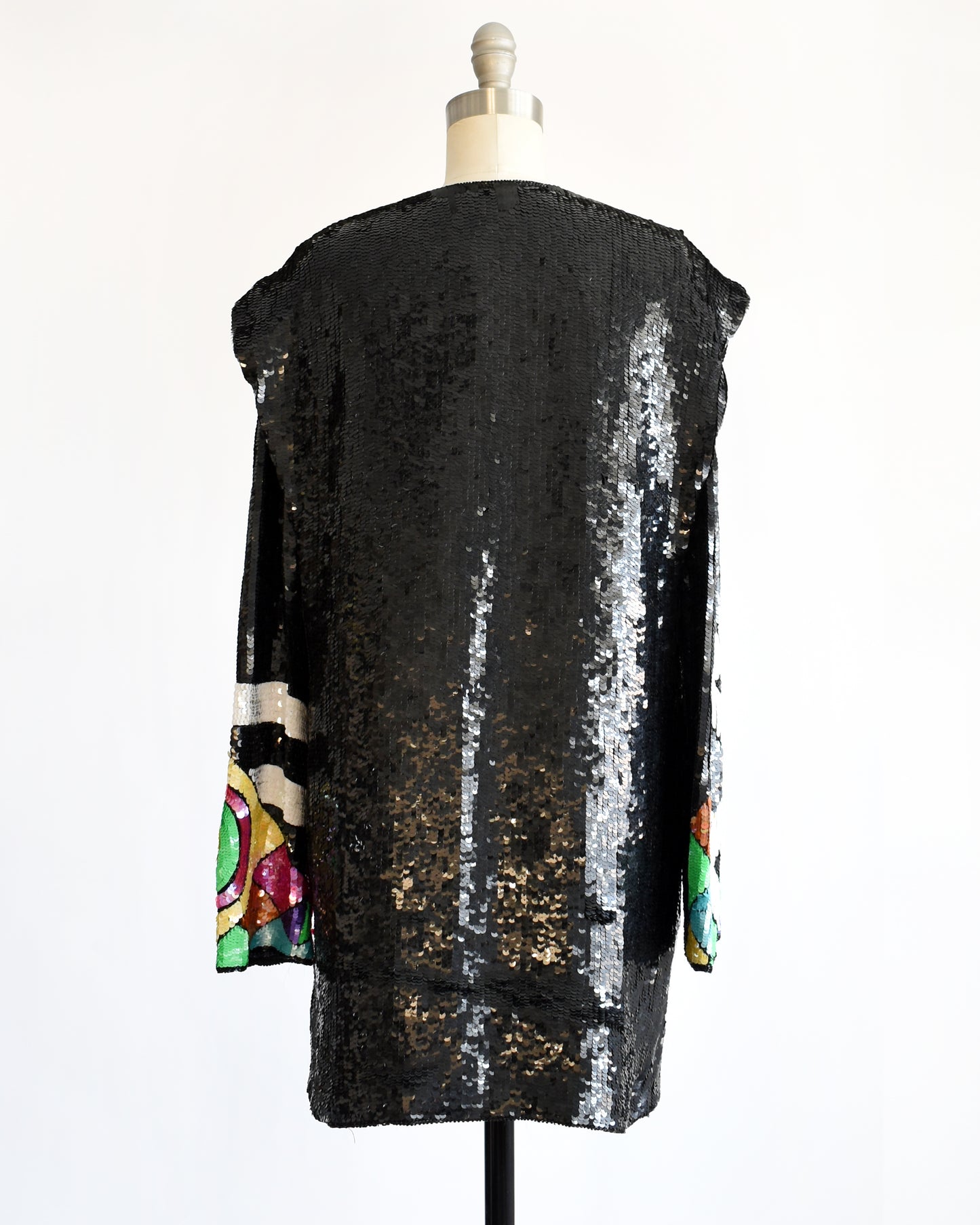 back view of a vintage 1980s 1990s black sequin cardigan jacket with colorful abstract patterns on a mannequin against a white background