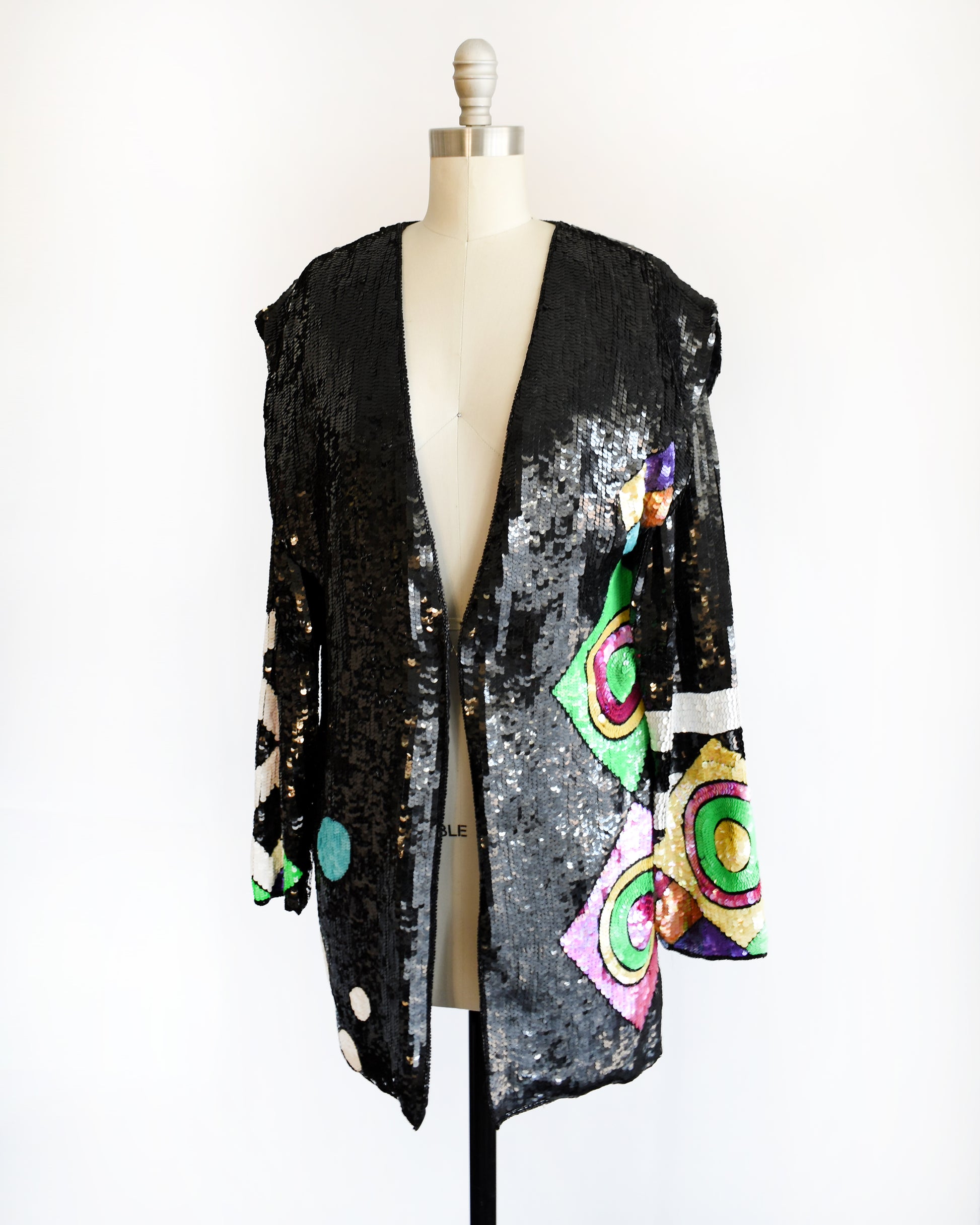 side front view of a vintage 1980s 1990s black sequin cardigan jacket with colorful abstract patterns on a mannequin against a white background