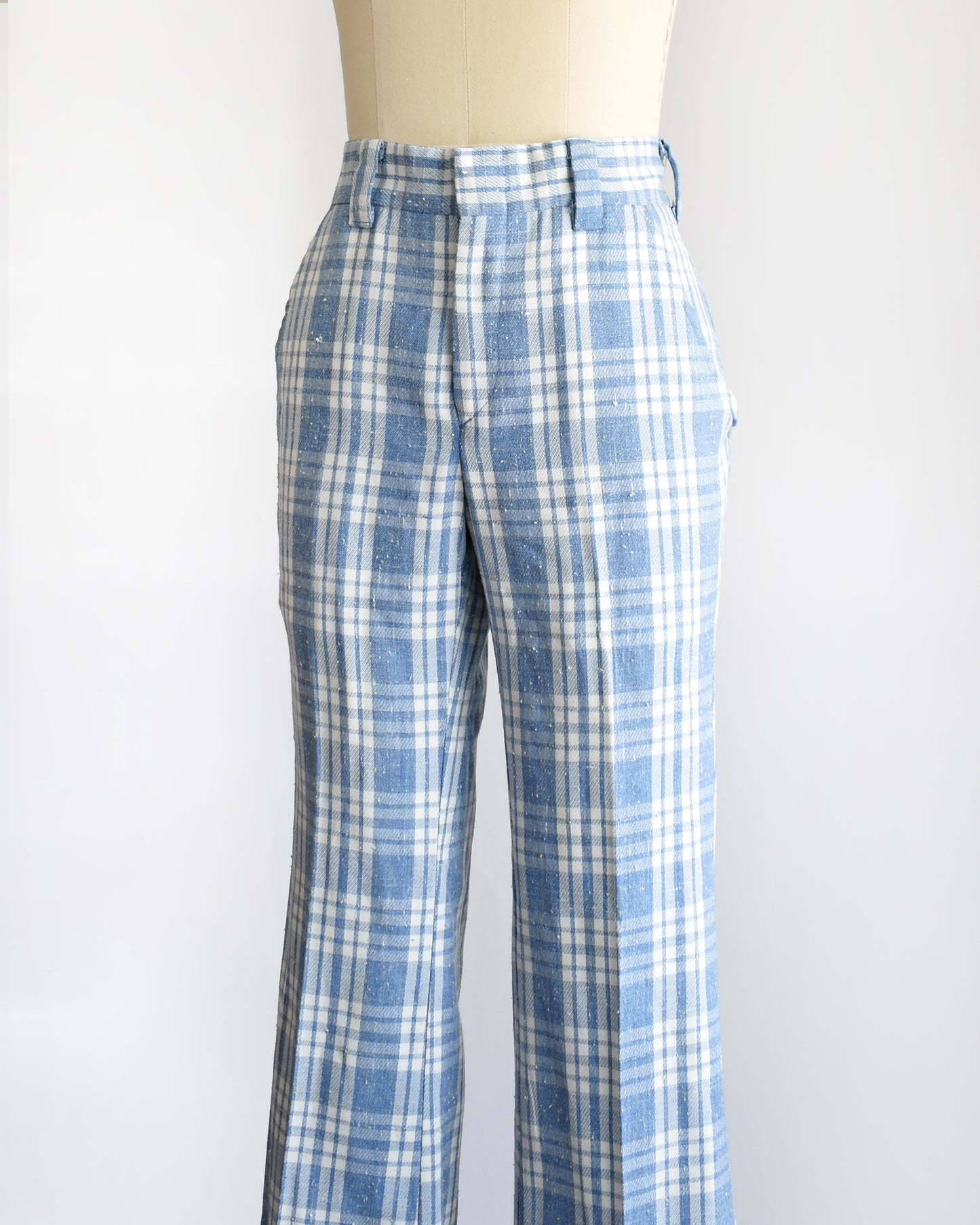 side front view of vintage 1970s blue and white plaid wide-leg pants displayed on a cream dress form mannequin against a plain white background.