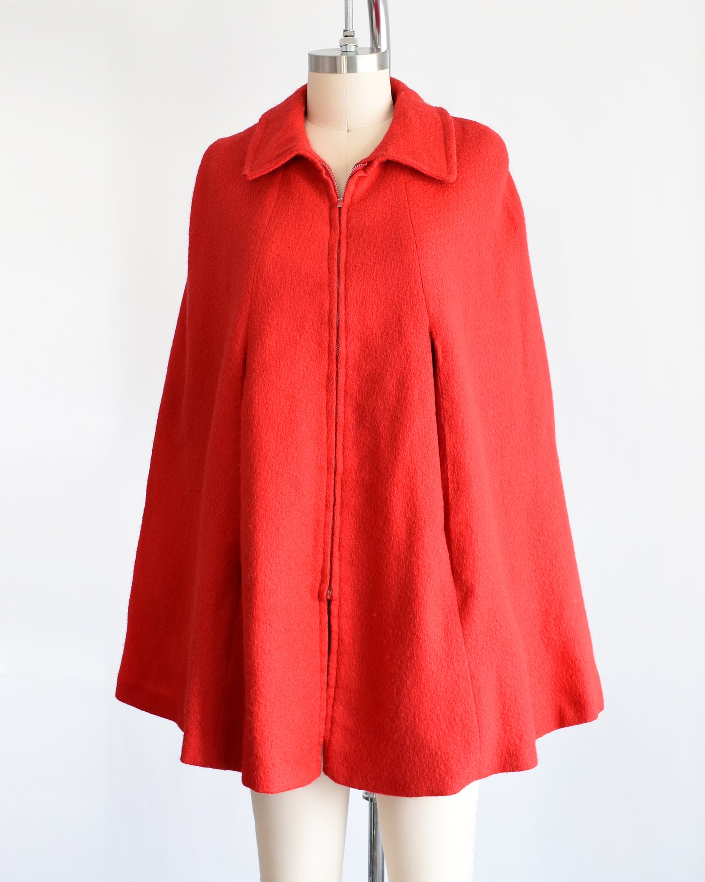 side front view of a vintage 1960s red cape with zip up front, front arm slits, and collared neckline.