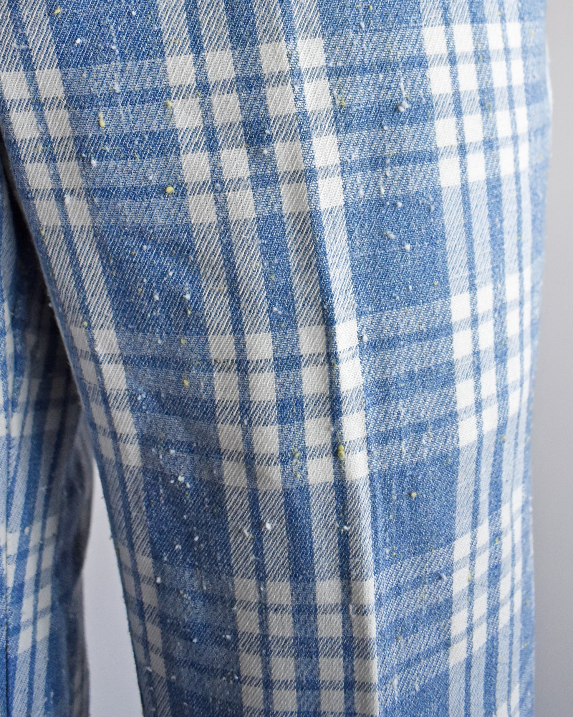 Close-up of blue and white plaid pants with small yellow and white specks scattered across it, likely lint or dust on the textile.
