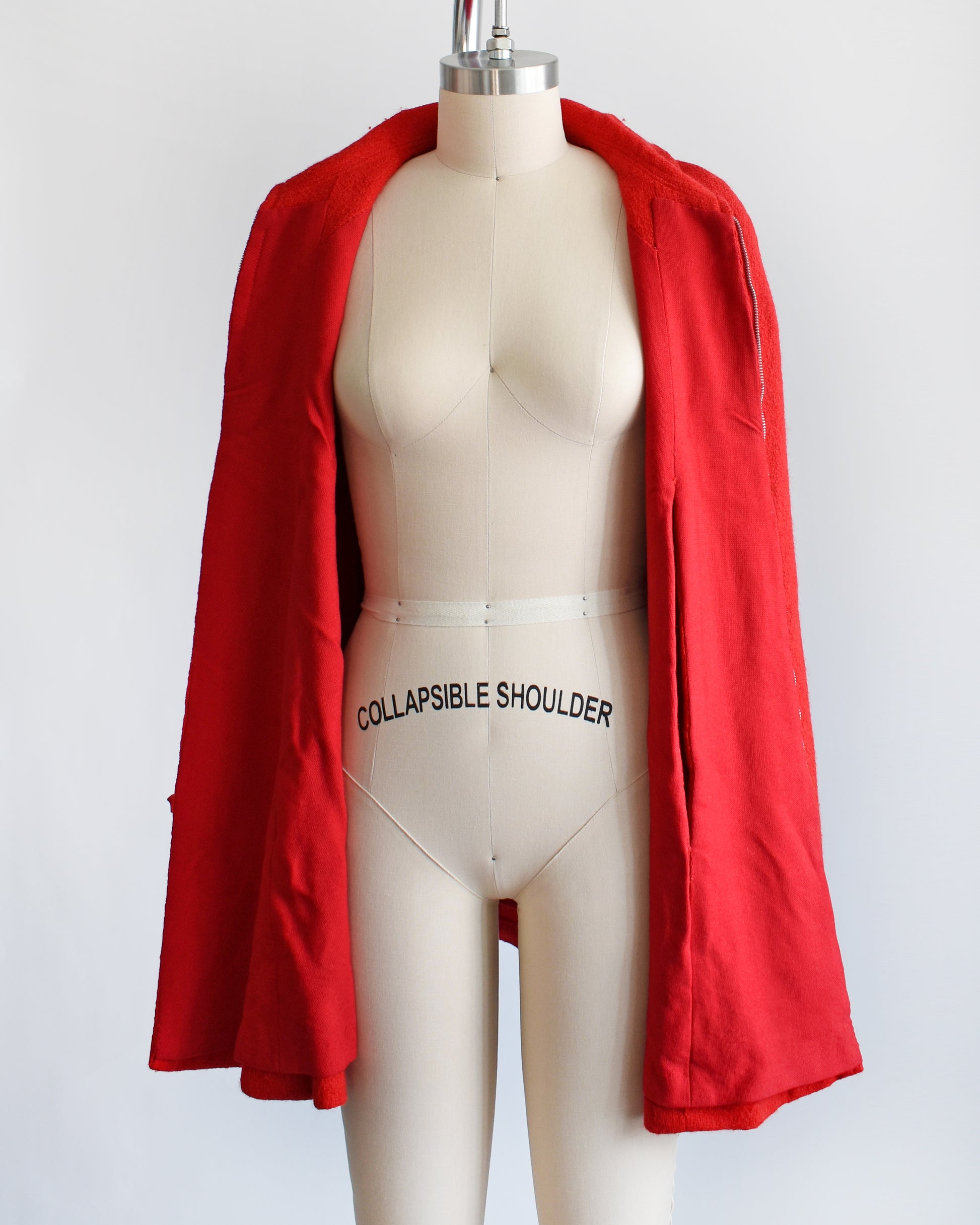 a vintage 1960s red cape with zip up front, front arm slits, and collared neckline. the cape is unzipped and open in this photo which shows the red lining