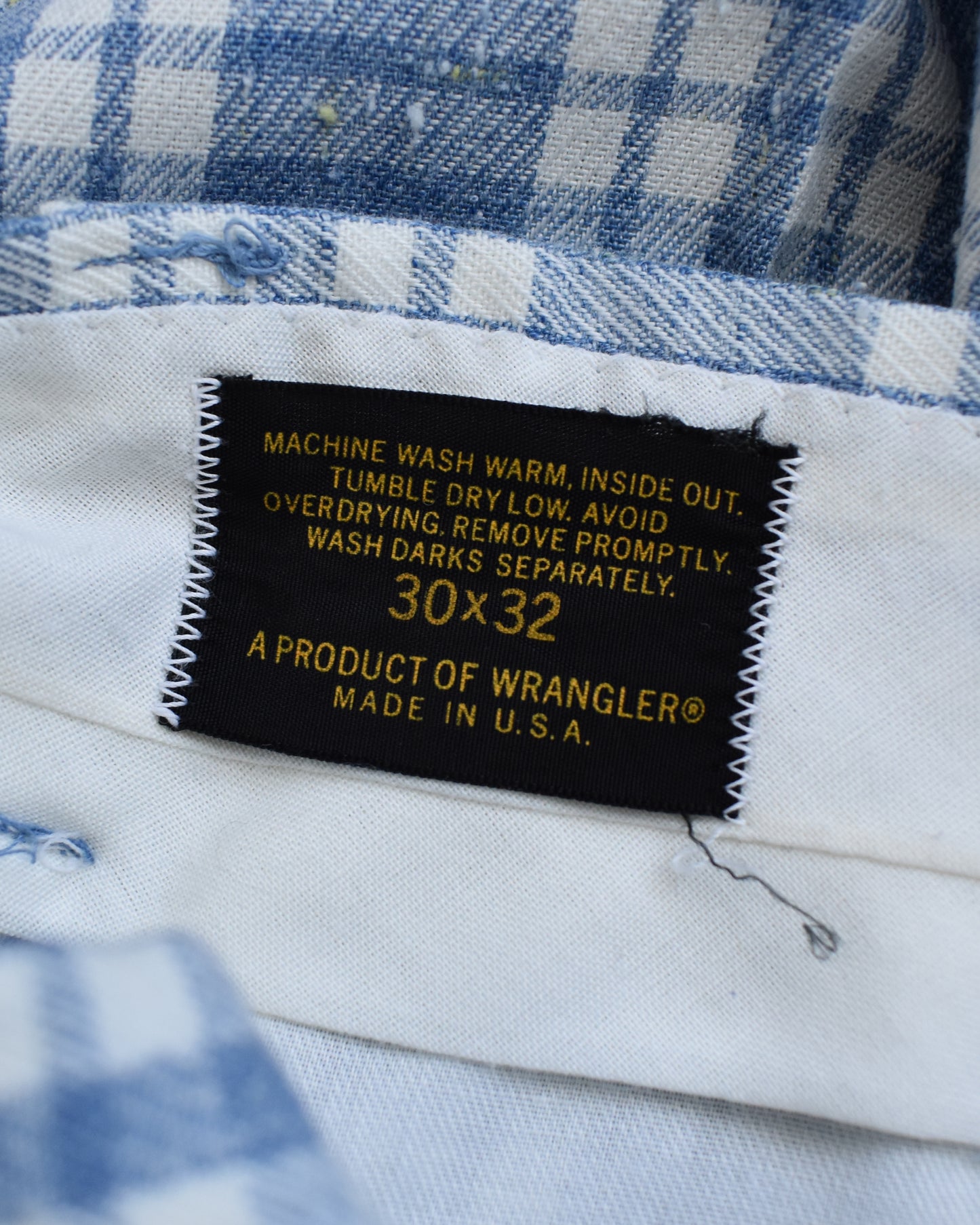 Close-up of a black sewn-in label with yellow text reading '30x32 A PRODUCT OF WRANGLER MADE IN U.S.