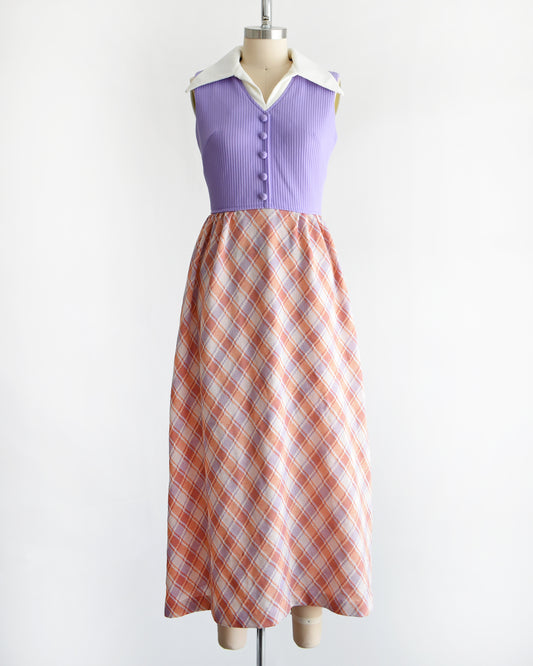 a vintage 1970s sleeveless maxi dress displayed on a mannequin against a plain white background. The dress features a lavender purple ribbed bodice with a white collar and button details, paired with a pleated skirt in a peach, orange, and white plaid pattern.