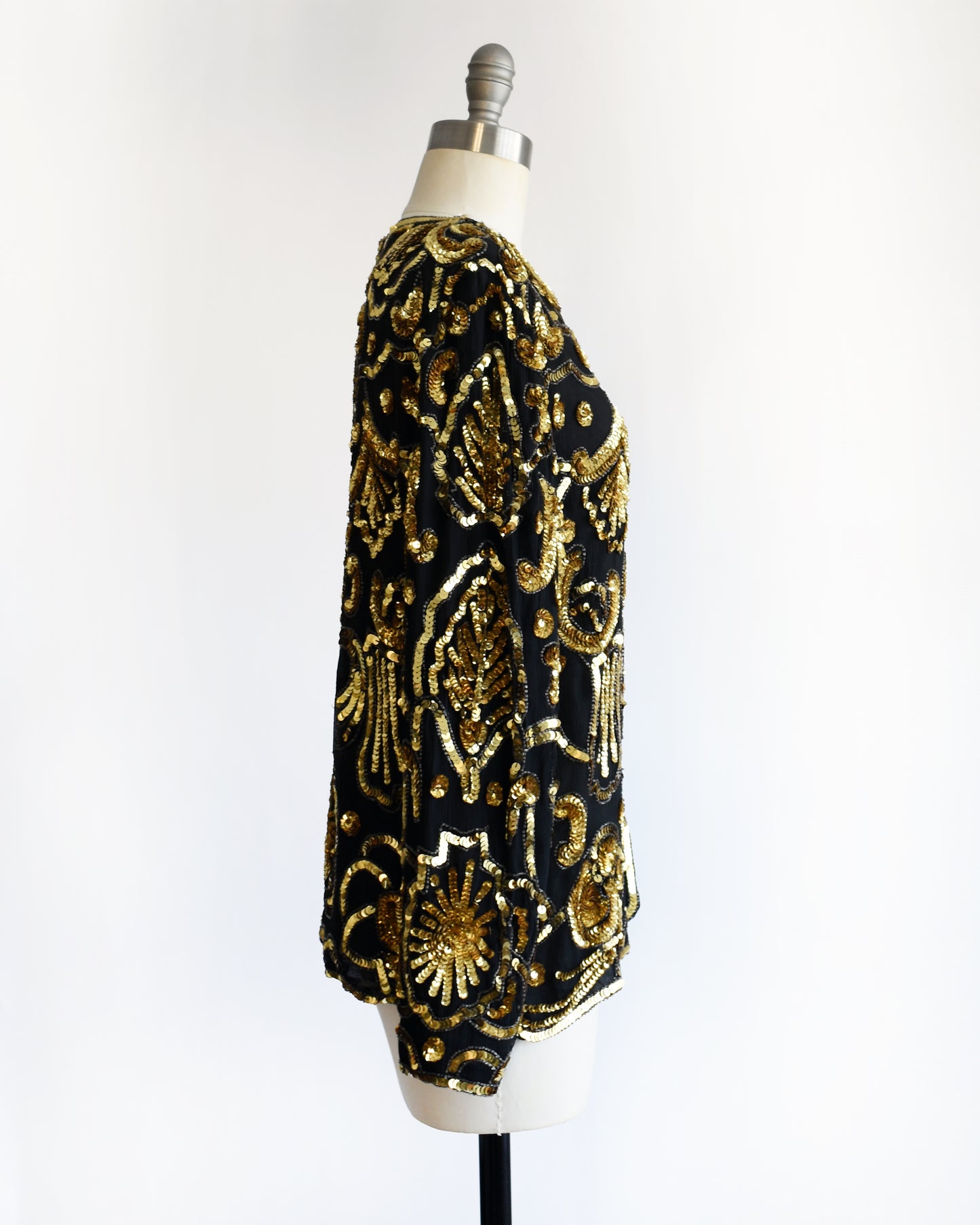 side view of a black and gold vintage sequin jacket on a mannequin against a white background