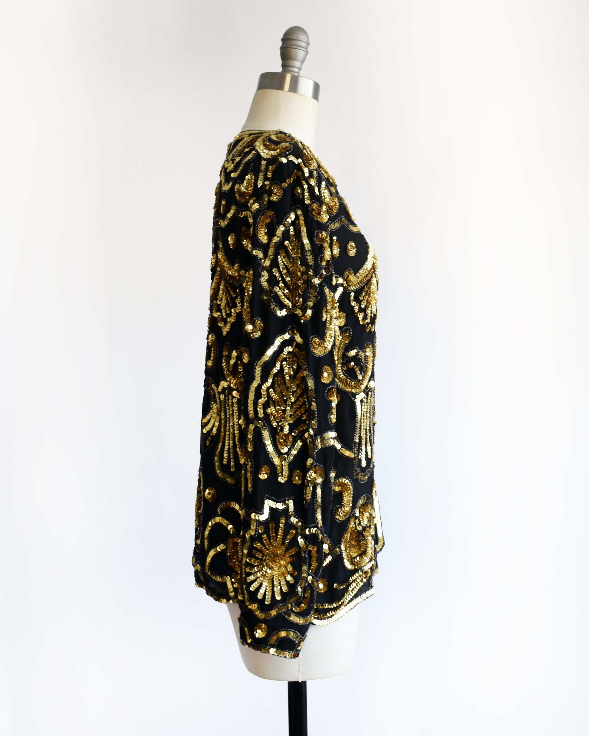 side view of a black and gold vintage sequin jacket on a mannequin against a white background