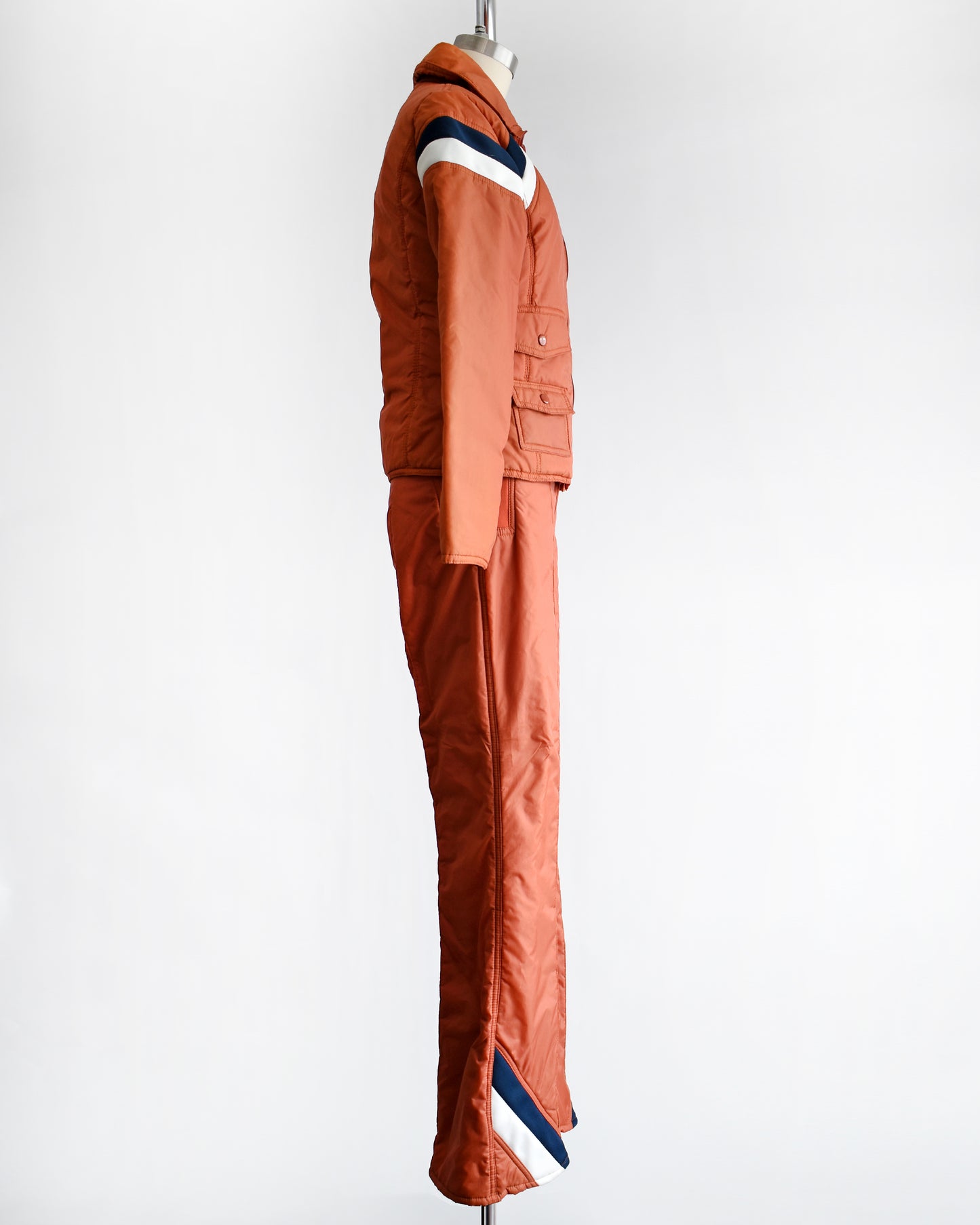 side view of a vintage 1970s orange winter ski suit on a mannequin against a white background