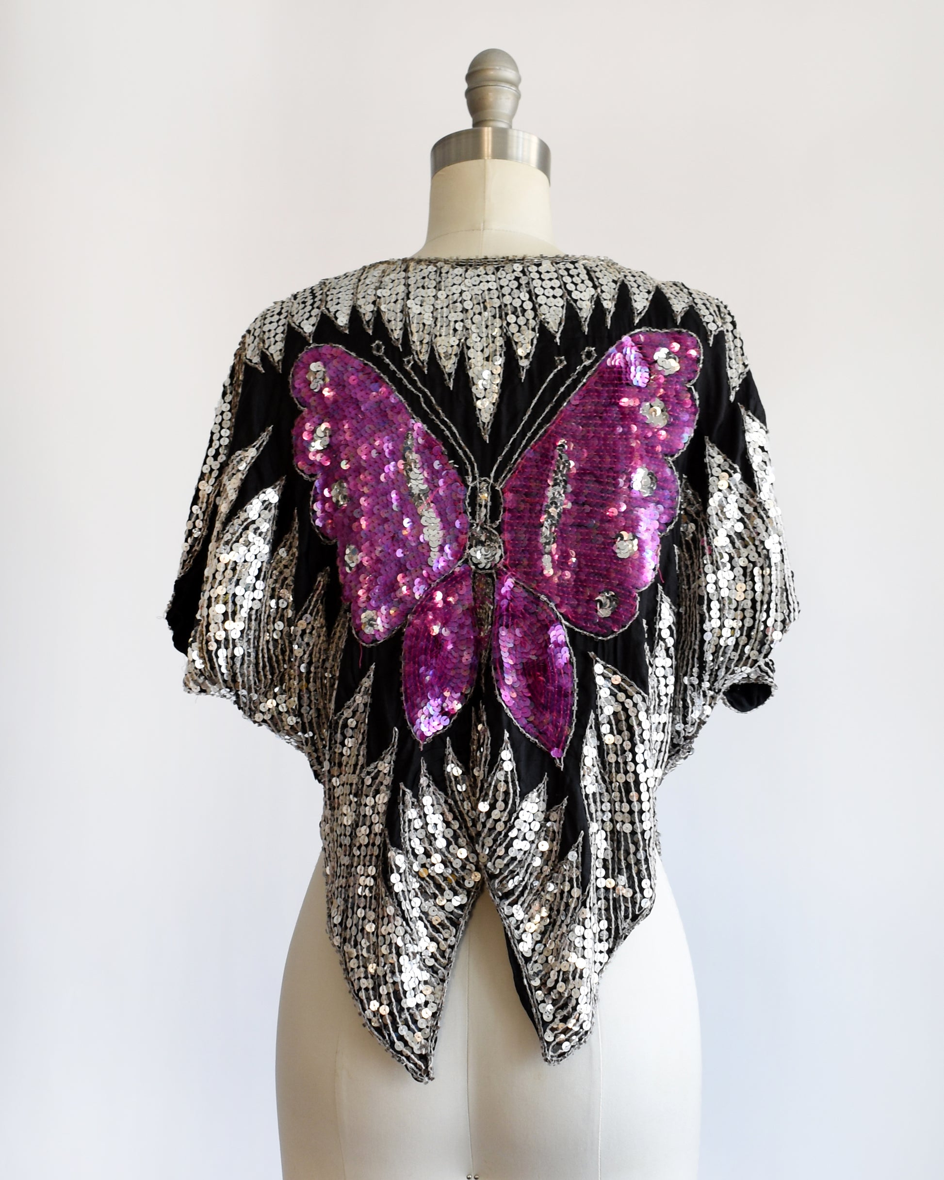 back view of a vintage 1970s / 1980s sequined top with butterfly design on a mannequin against a white background