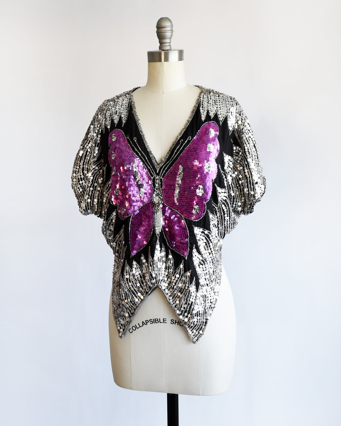 side front view of a vintage 1970s / 1980s sequined top with butterfly design on a mannequin against a white background