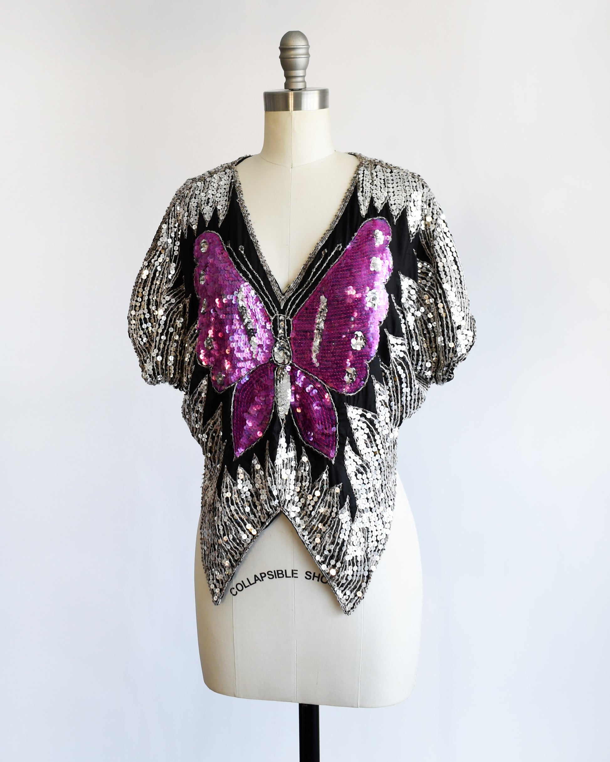 side front view of a vintage 1970s / 1980s sequined top with butterfly design on a mannequin against a white background