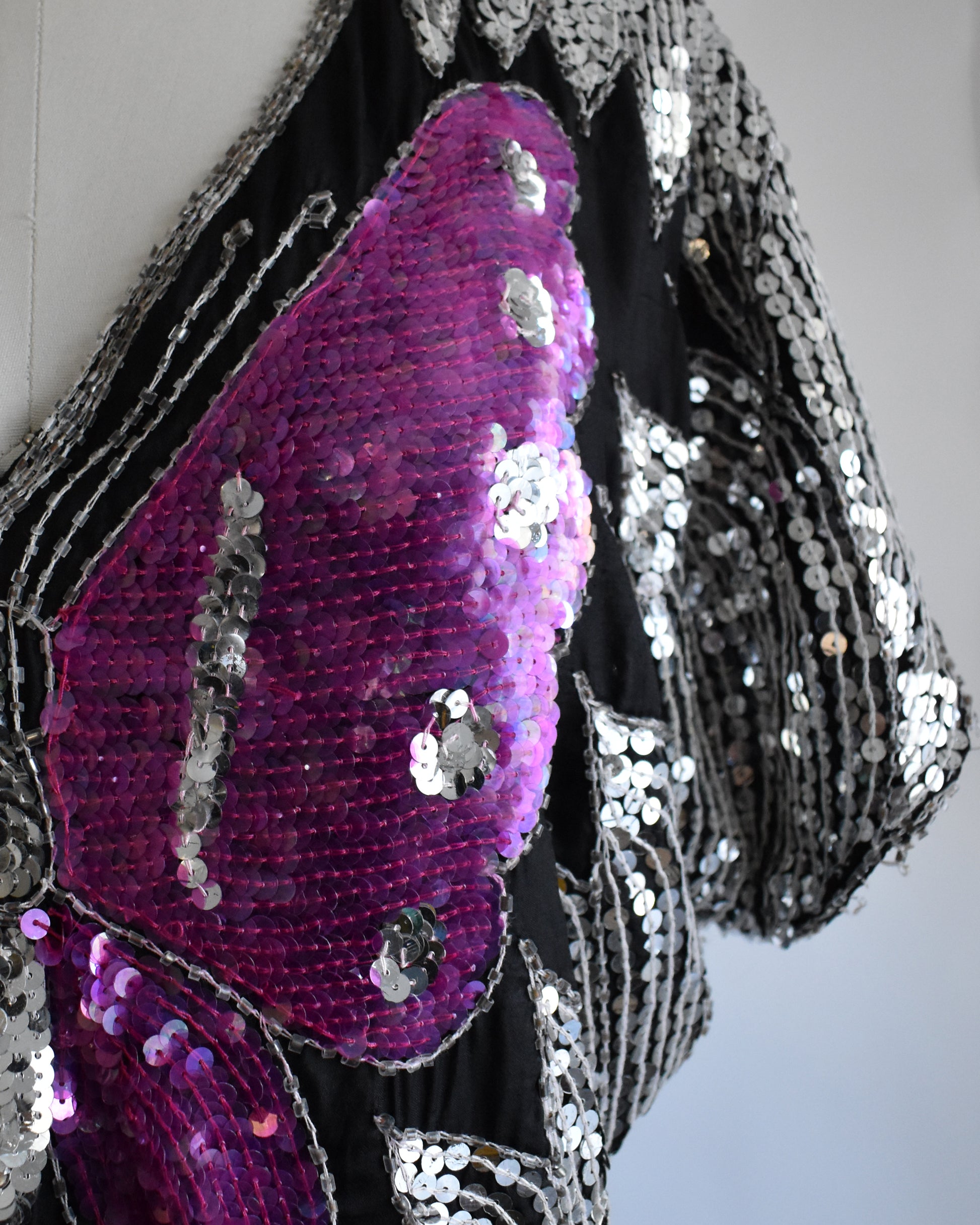 close up of the butterfly wing on a vintage 1970s / 1980s sequined top with butterfly design on a mannequin against a white background
