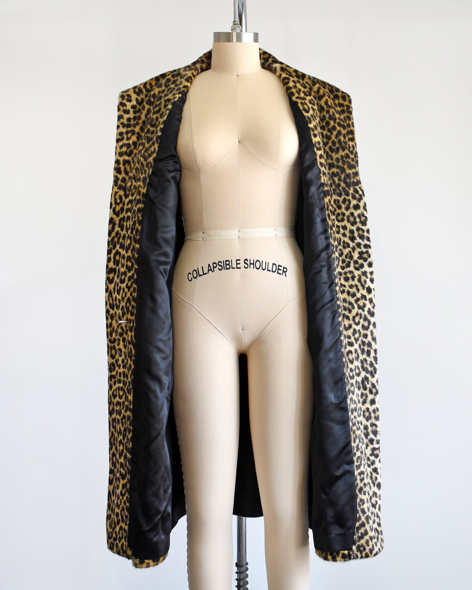 A vintage 1960s faux fur leopard print coat on a dress form. The coat is open showing the black lining inside.