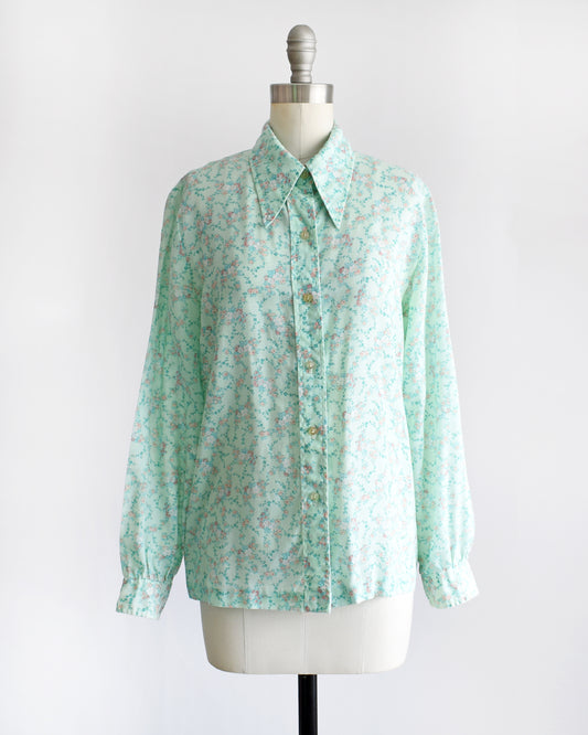 a vintage 1970s long-sleeve button-up blouse with a light mint green and pink floral pattern, displayed on a cream dress form mannequin against a white background.