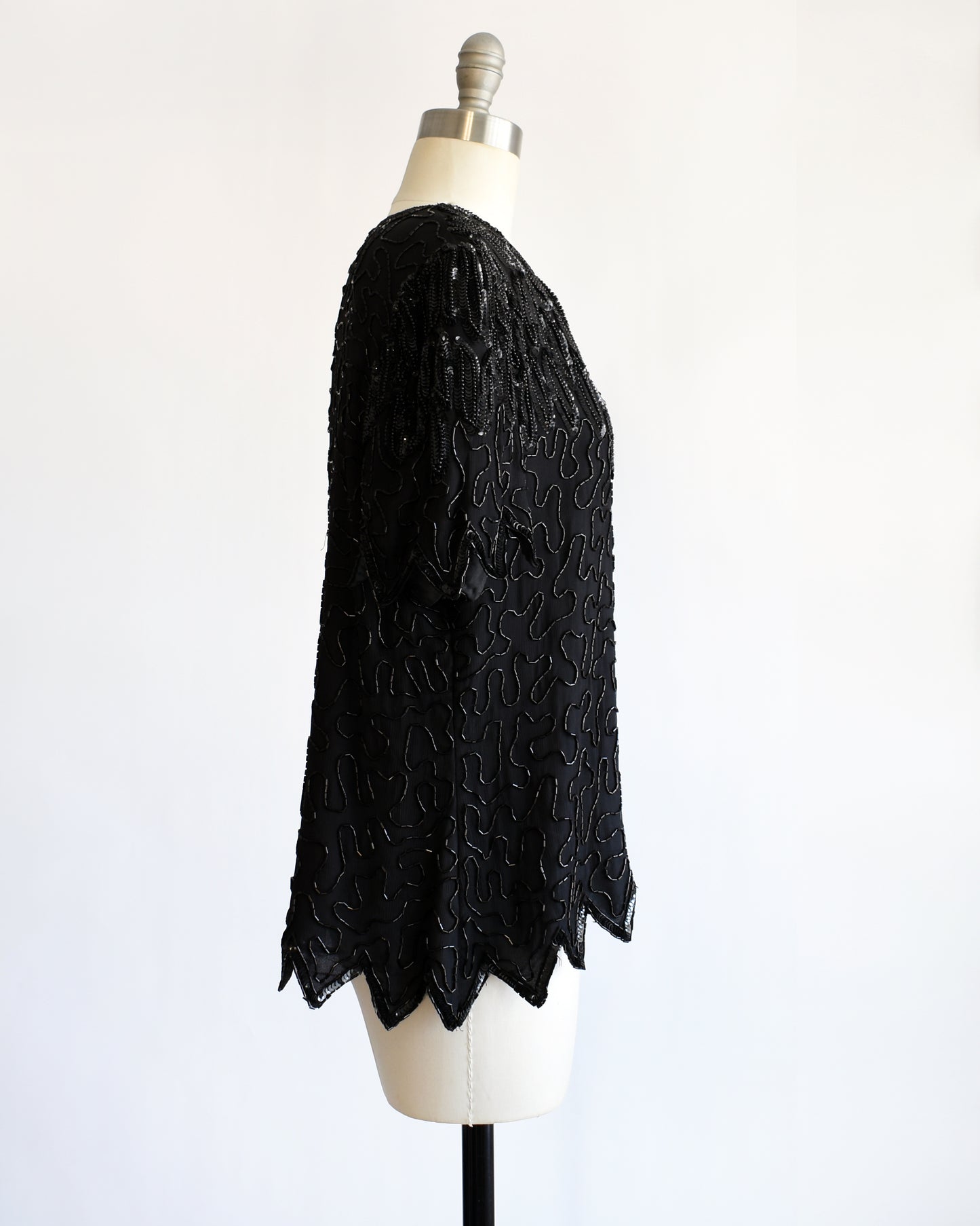 side view of a vintage 1980s black sequin and beaded top on a mannequin against a white background