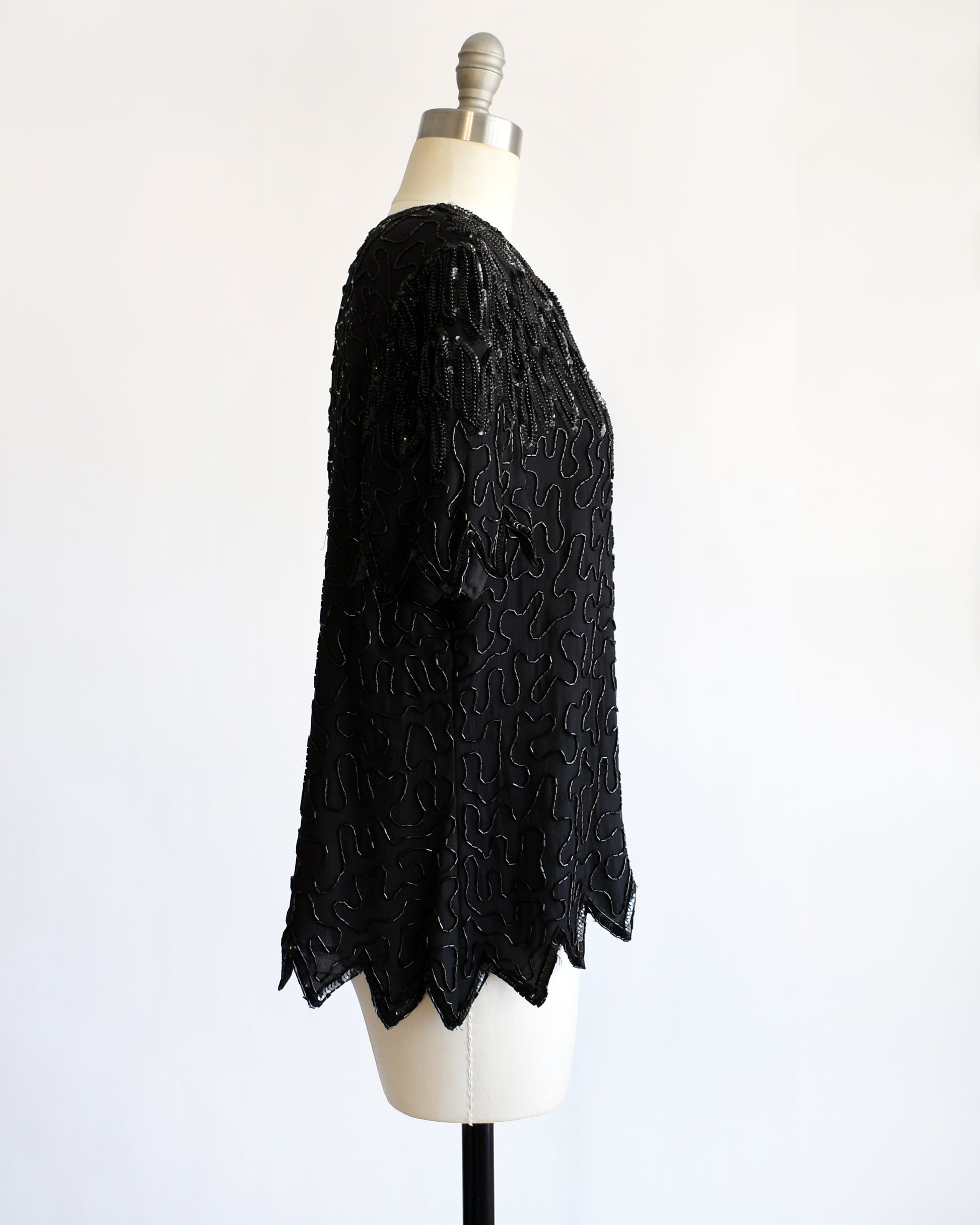 side view of a vintage 1980s black sequin and beaded top on a mannequin against a white background