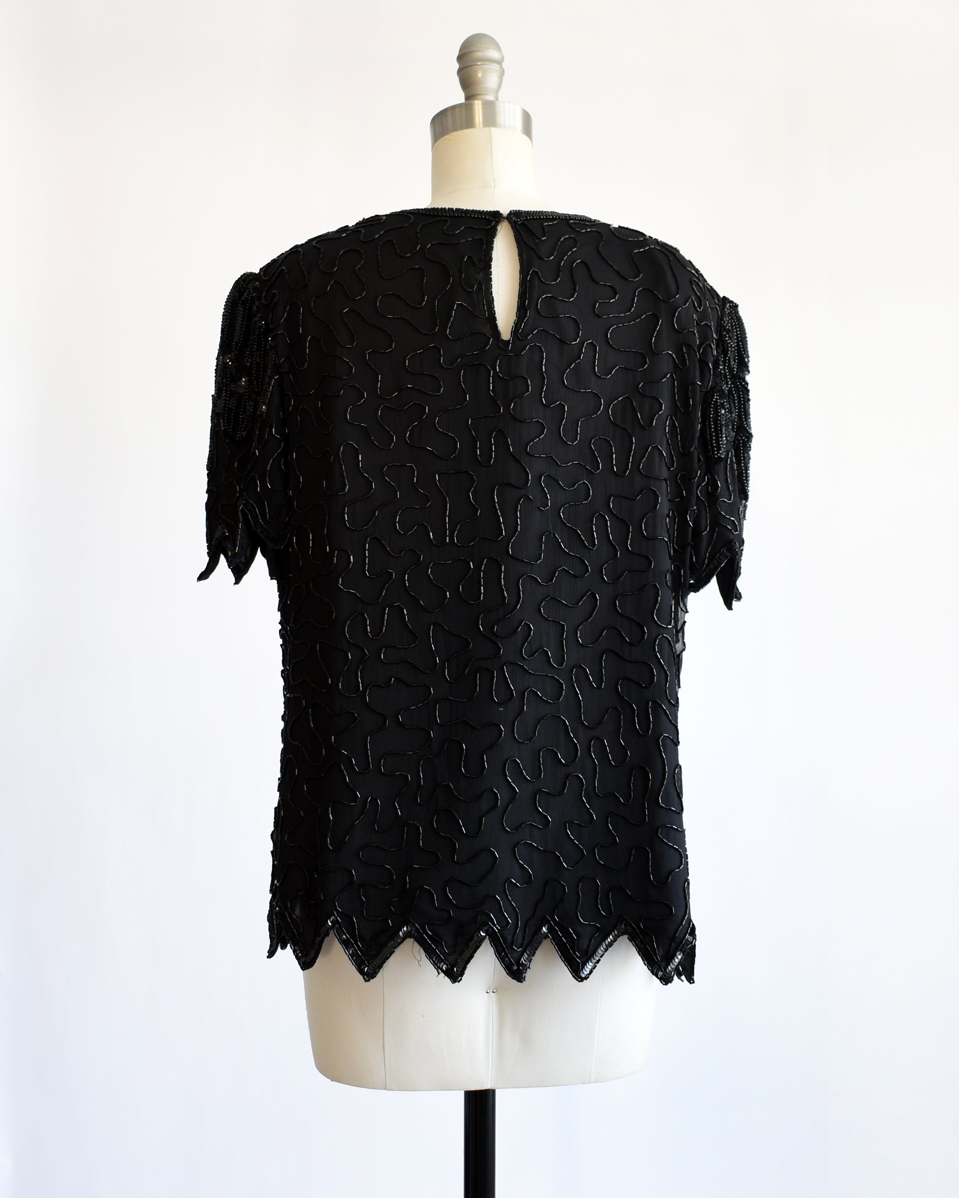 back view of a vintage 1980s black sequin and beaded top on a mannequin against a white background