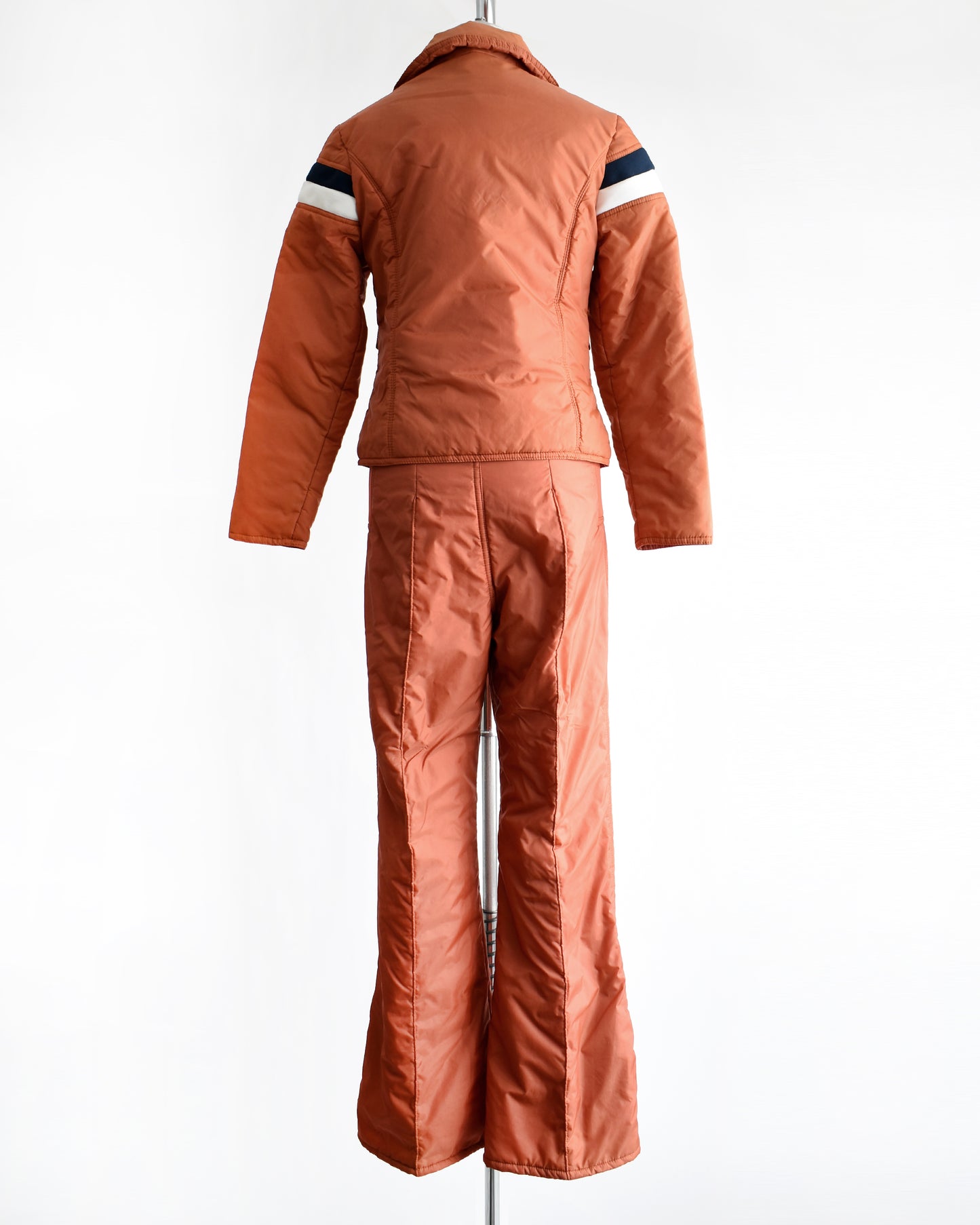 back view of a vintage 1970s orange winter ski suit on a mannequin against a white background
