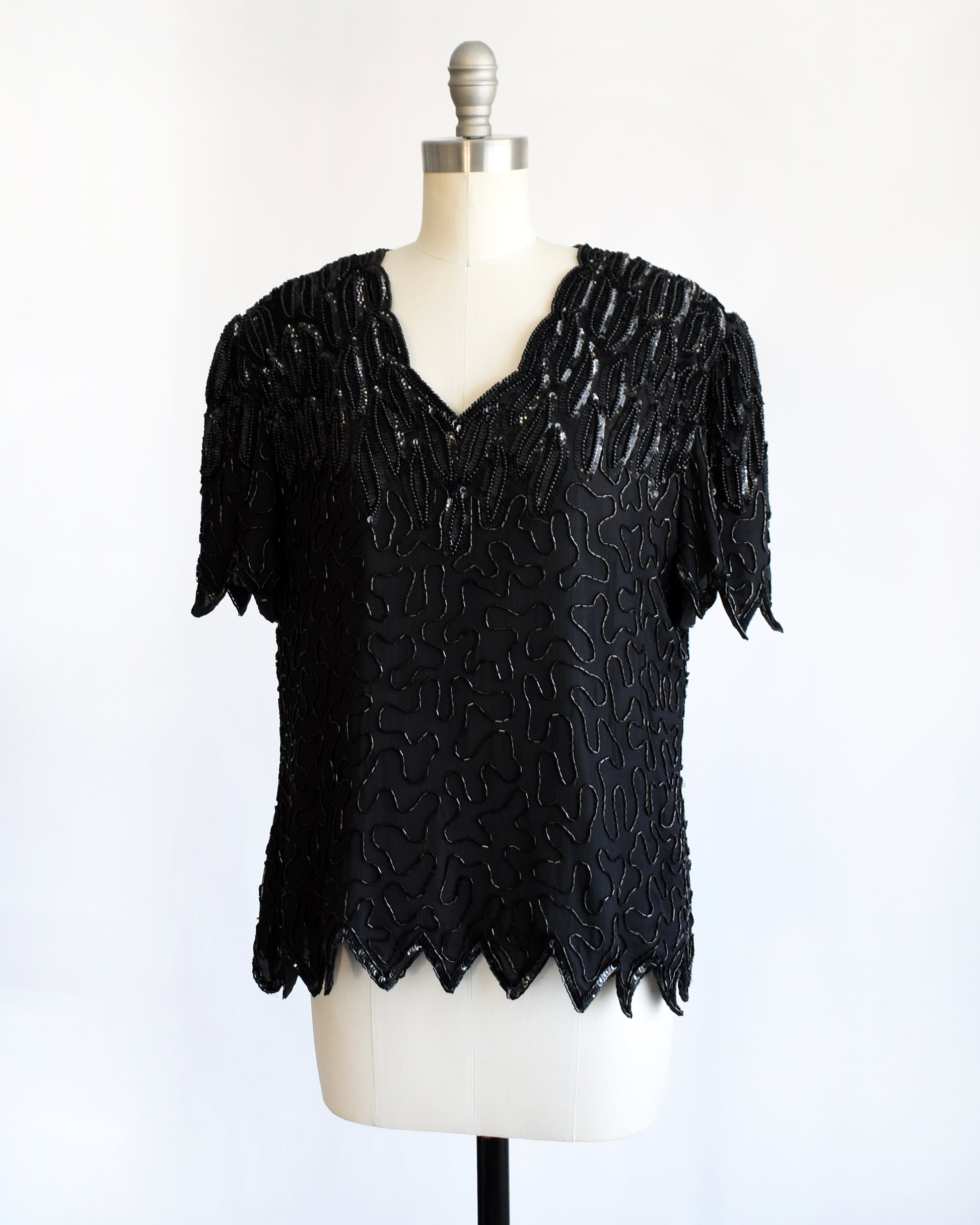 side front view of a vintage 1980s black sequin and beaded top on a mannequin against a white background
