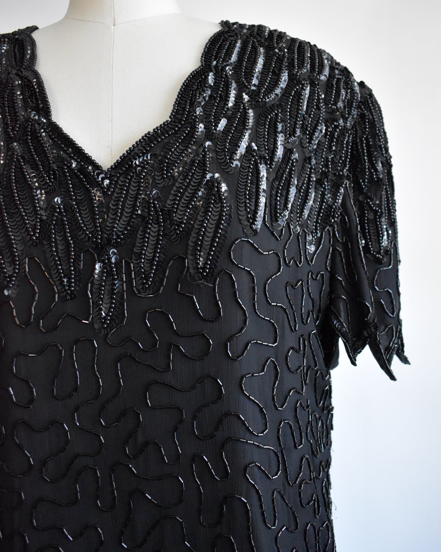 close up of the beaded and sequin detail on a vintage 1980s black sequin and beaded top on a mannequin against a white background