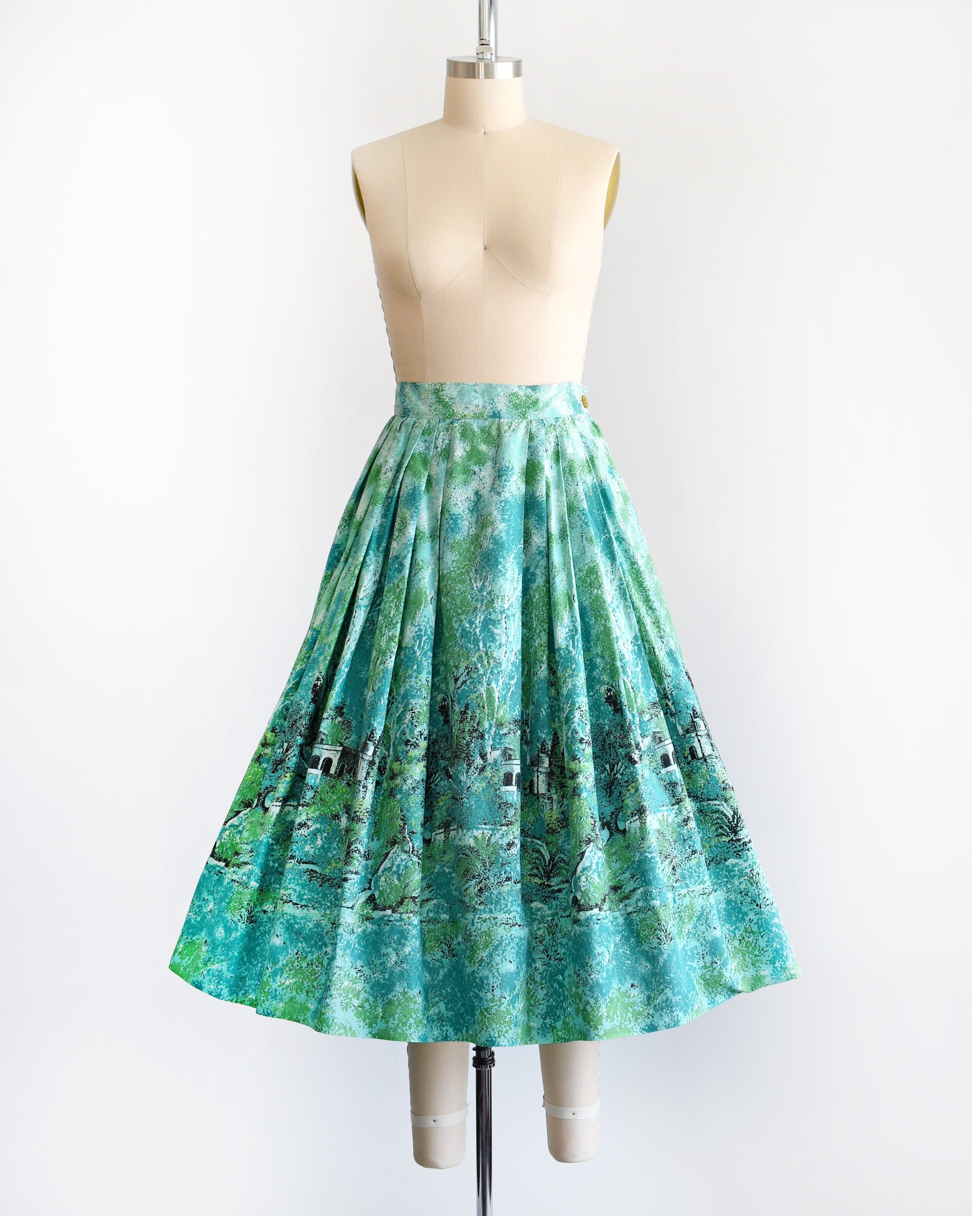 A vintage 1950s blue and green novelty print skirt that has a scenic forest and chateau border print scene.