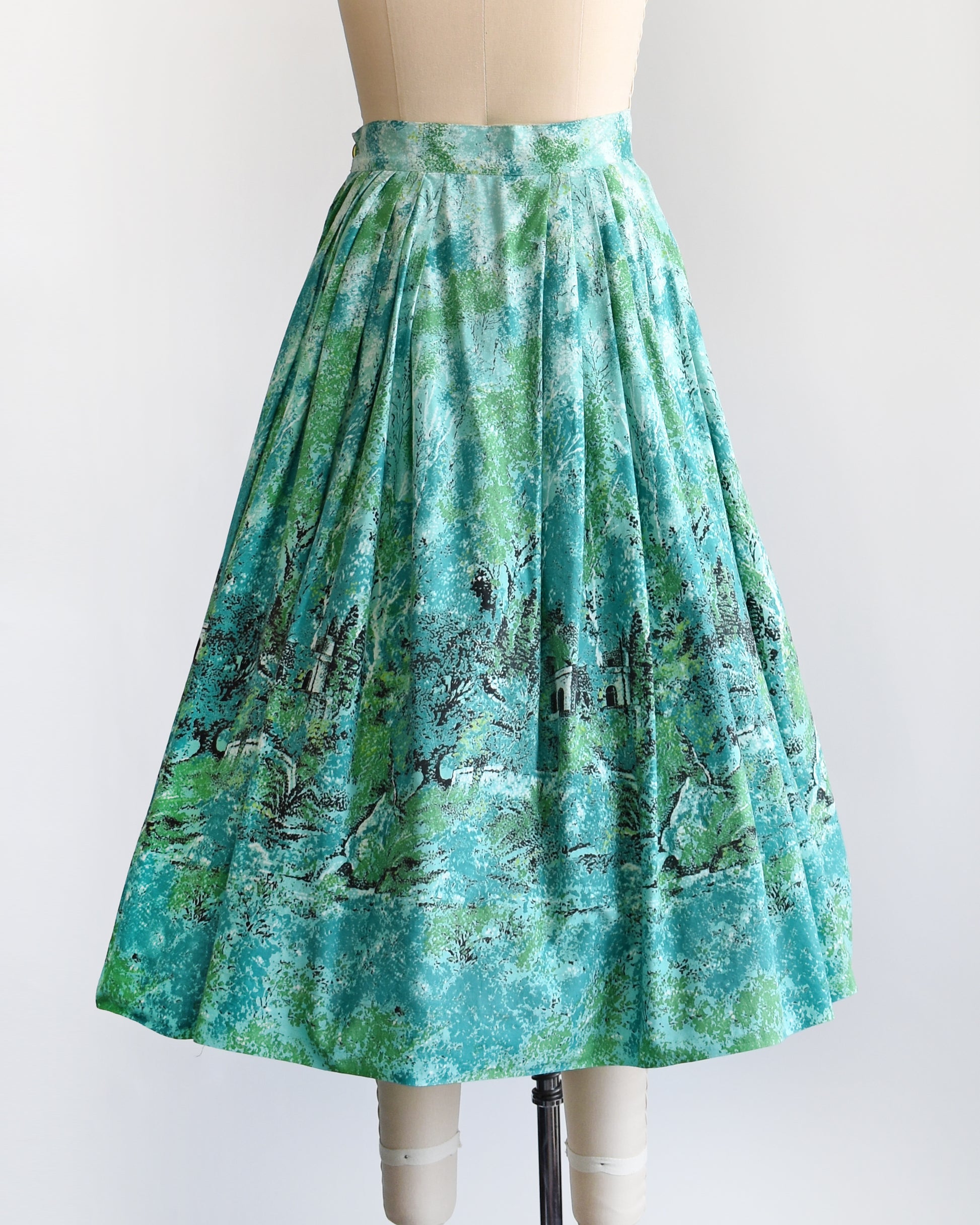 back view of a vintage 1950s blue and green novelty print skirt that has a scenic forest and chateau border print scene.