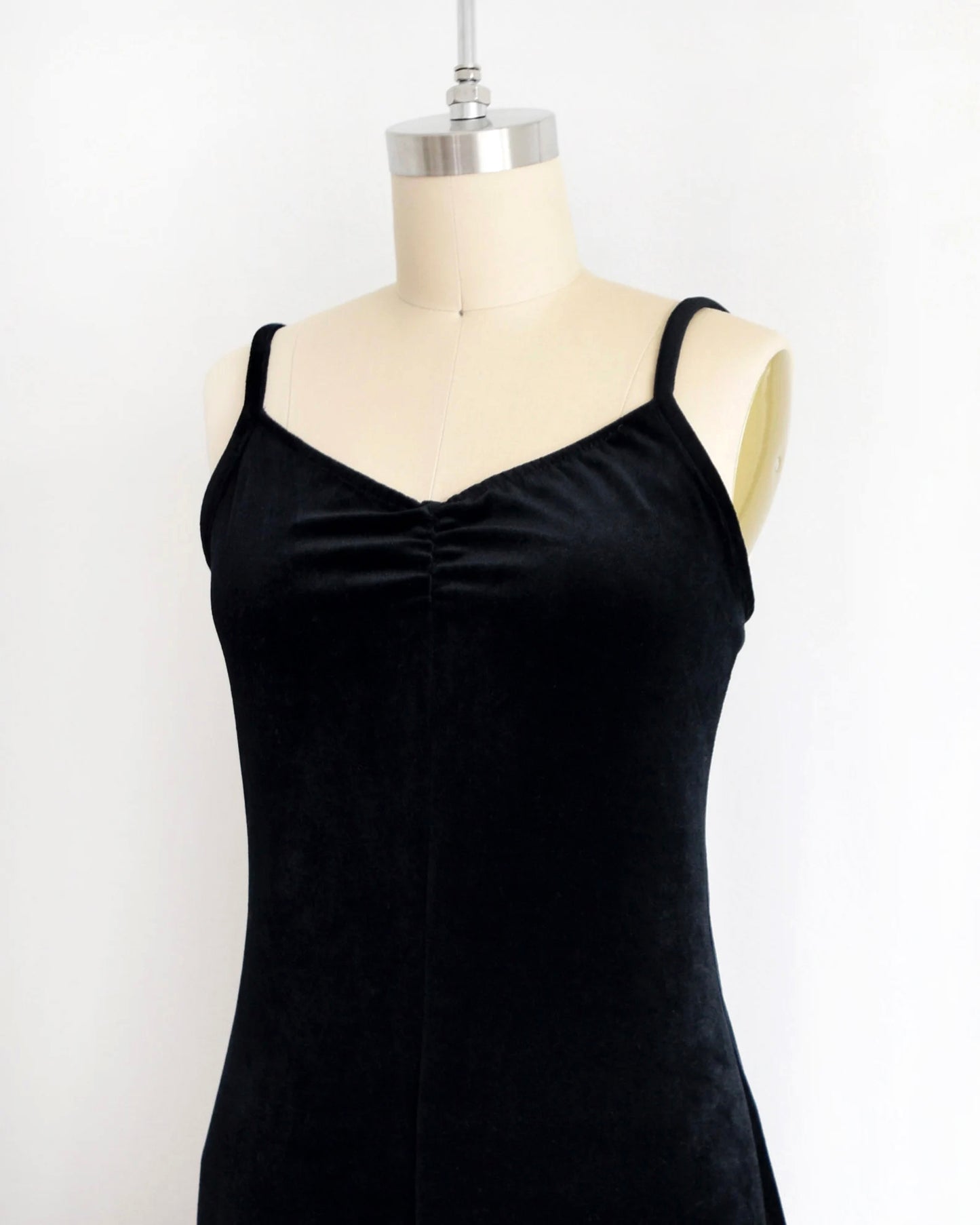 side front view of a black velvet jumpsuit displayed on a mannequin against a white wall
