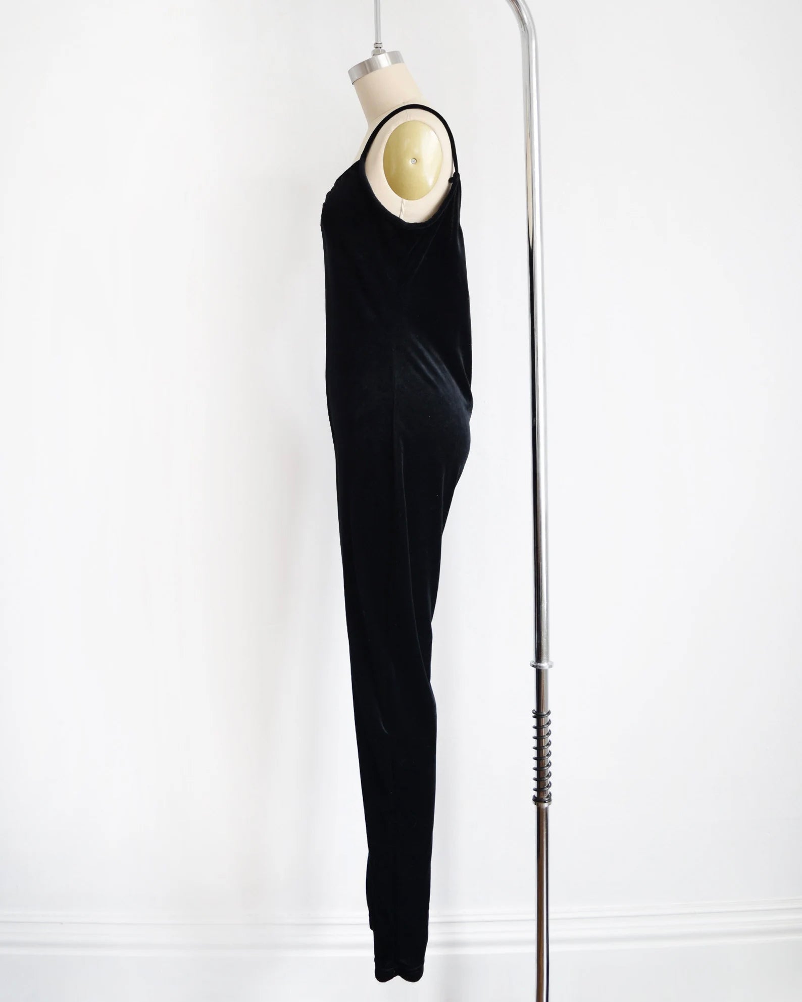 side view of ablack velvet jumpsuit displayed on a mannequin against a white wall, with a silver bar stand visible on the right side.