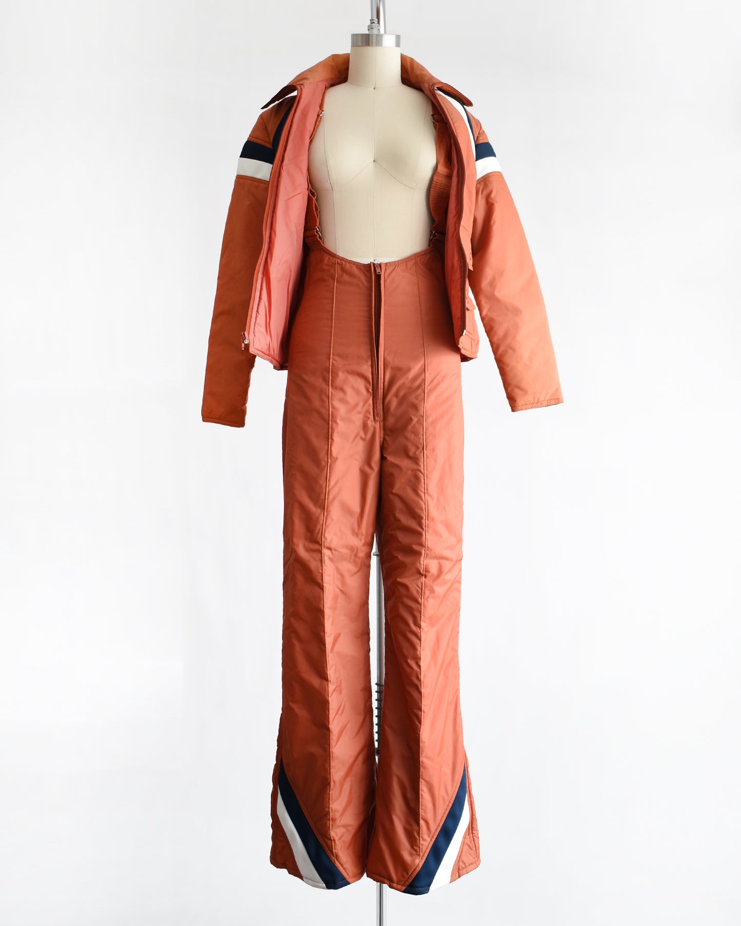 a vintage 1970s orange winter ski suit on a mannequin against a white background. the jacket is unzipped in this photo