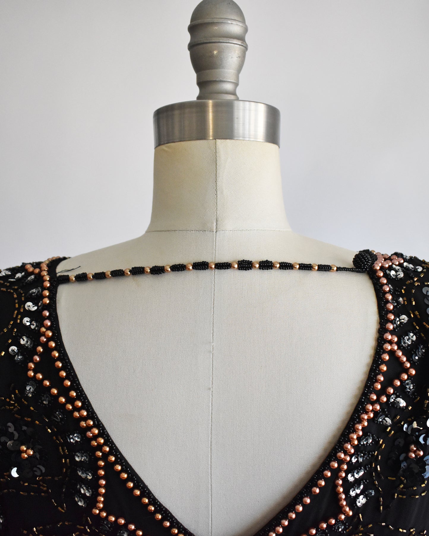 close up of the back beaded chain on a vintage 1980s black sequin and beaded top on a mannequin against a white background