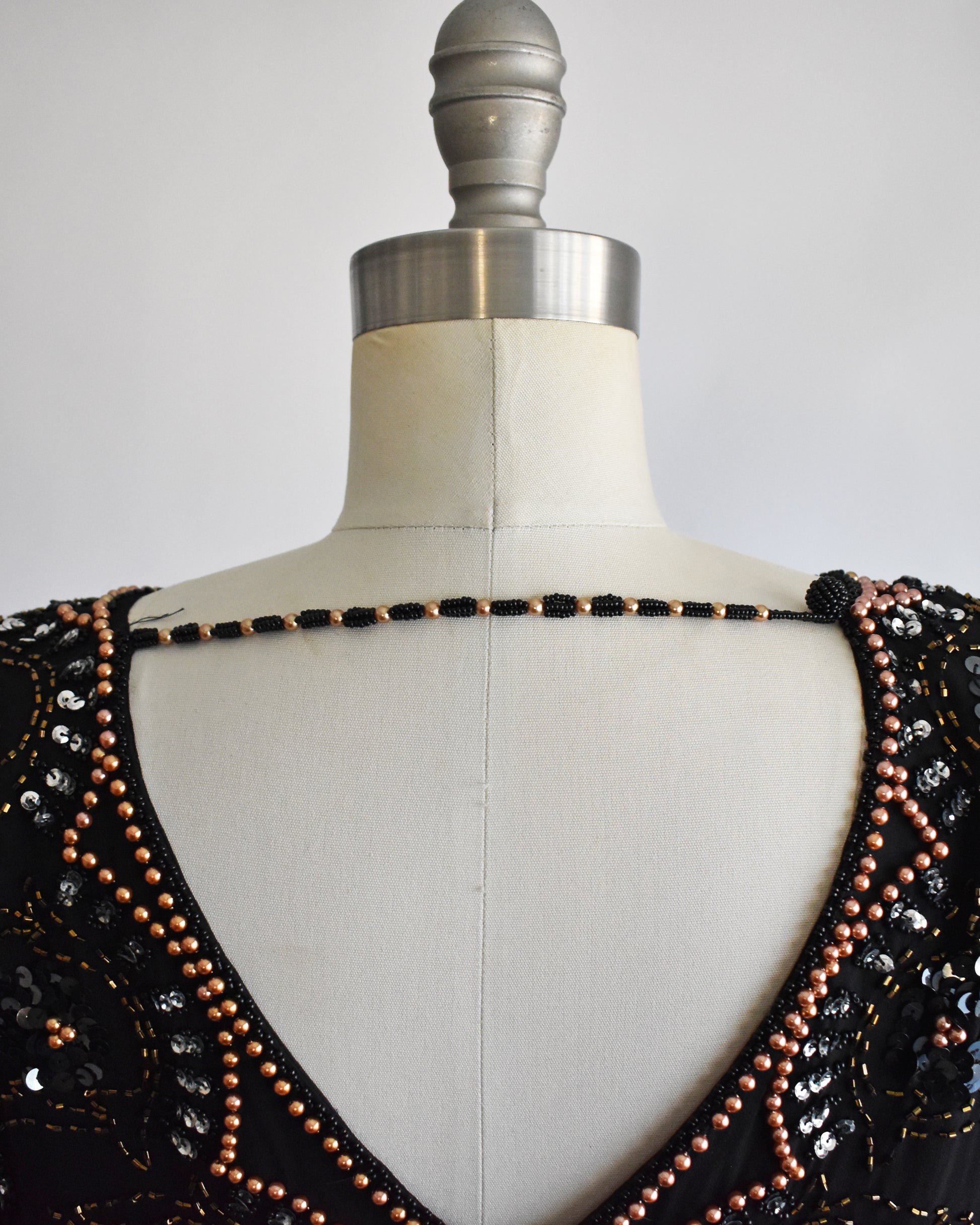 close up of the back beaded chain on a vintage 1980s black sequin and beaded top on a mannequin against a white background