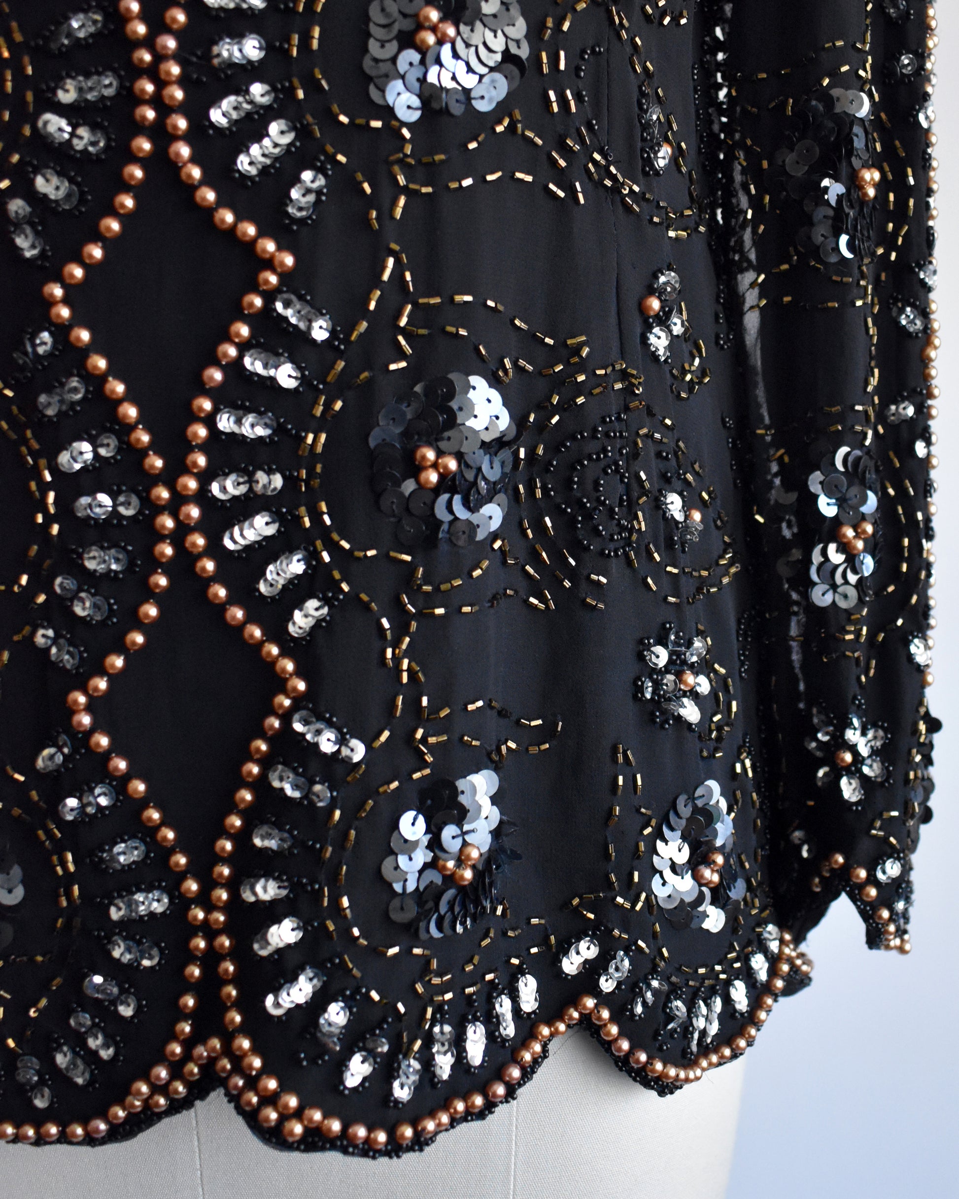 close up of the sequin and beaded detail on a vintage 1980s black sequin and beaded top on a mannequin against a white background