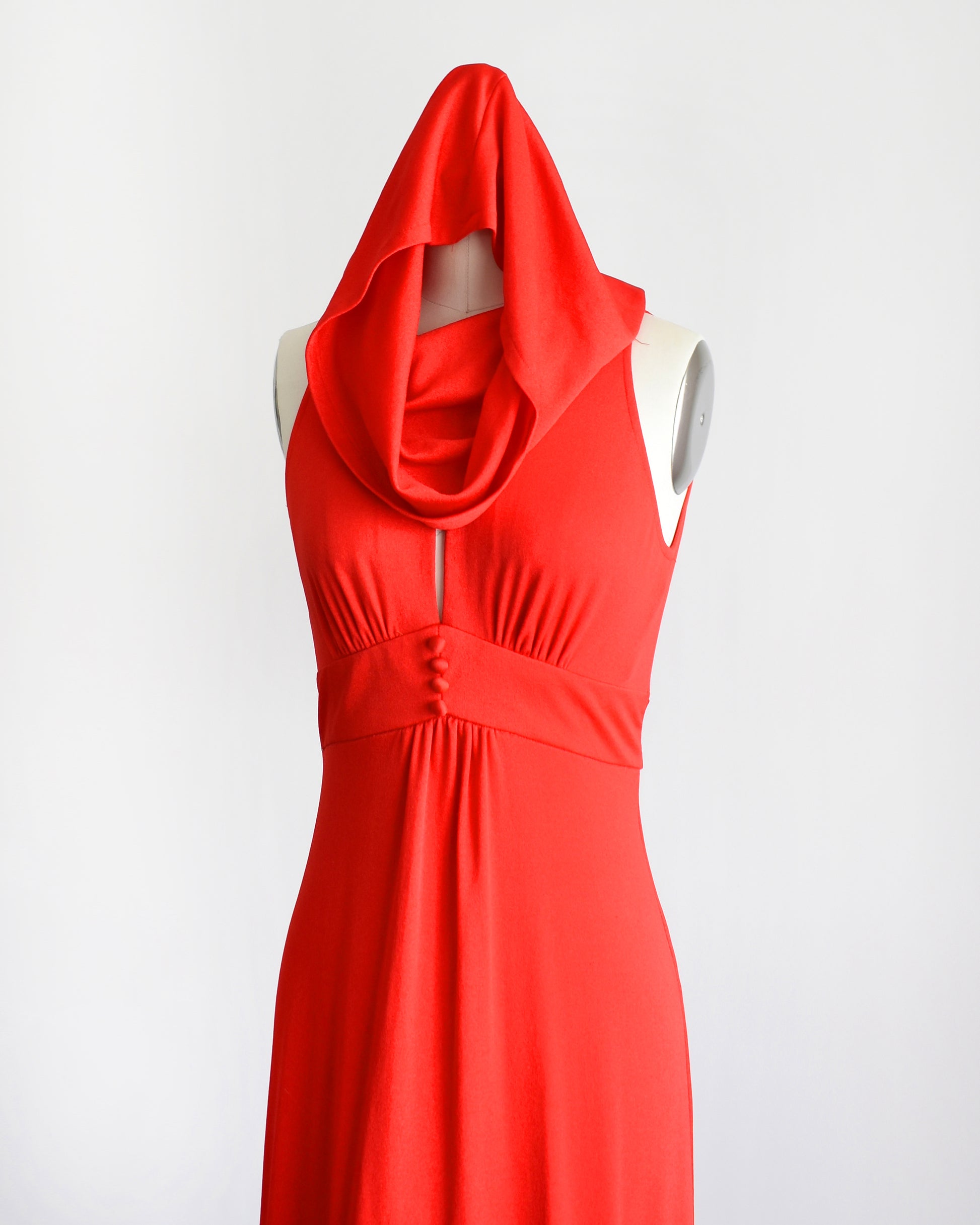 A bright red sleeveless halter-neck dress with a draped cowl hooded neckline and gathered waist, displayed on a white mannequin against a plain white background.