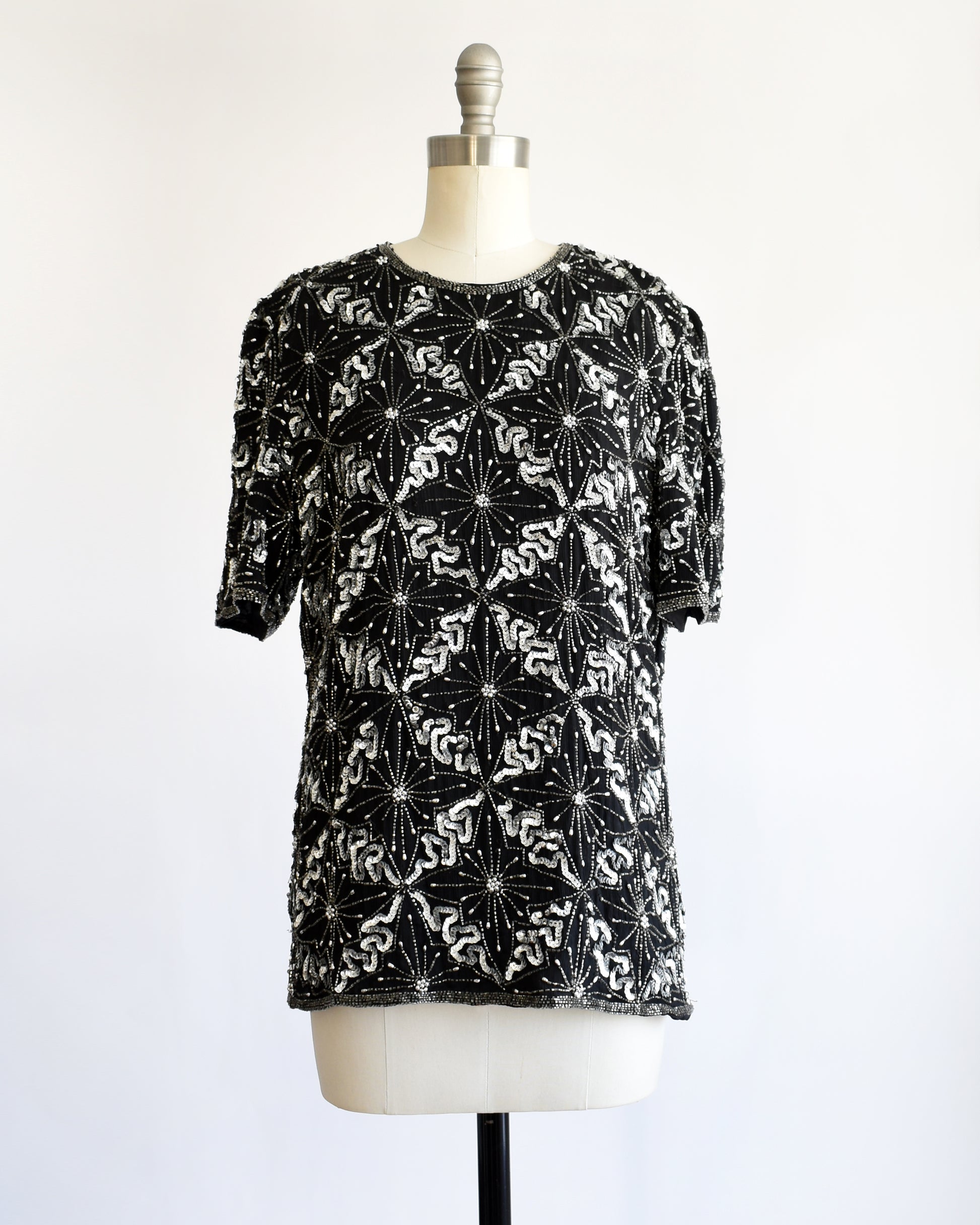 a vintage 1980s black and silver sequin beaded patterned top on a mannequin against a white background