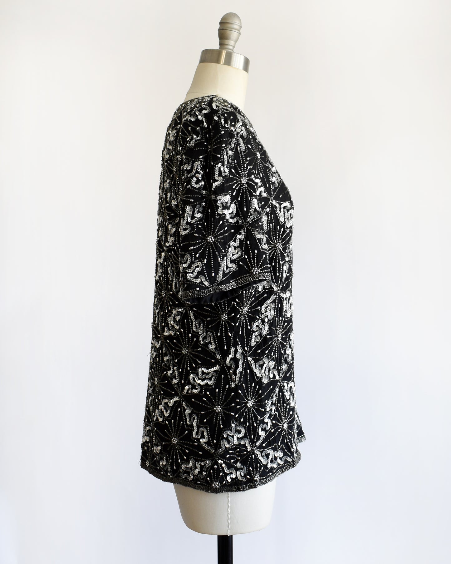 side view of a vintage 1980s black and silver sequin beaded patterned top on a mannequin against a white background 