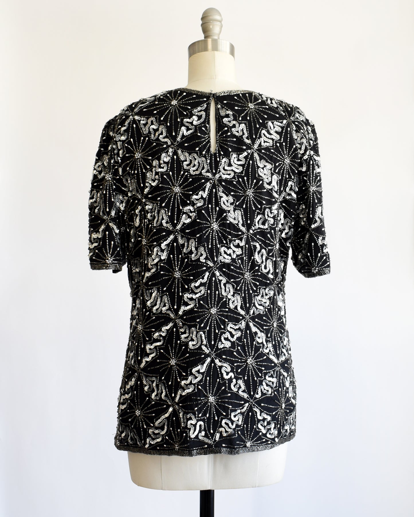 back view of a vintage 1980s black and silver sequin beaded patterned top on a mannequin against a white background