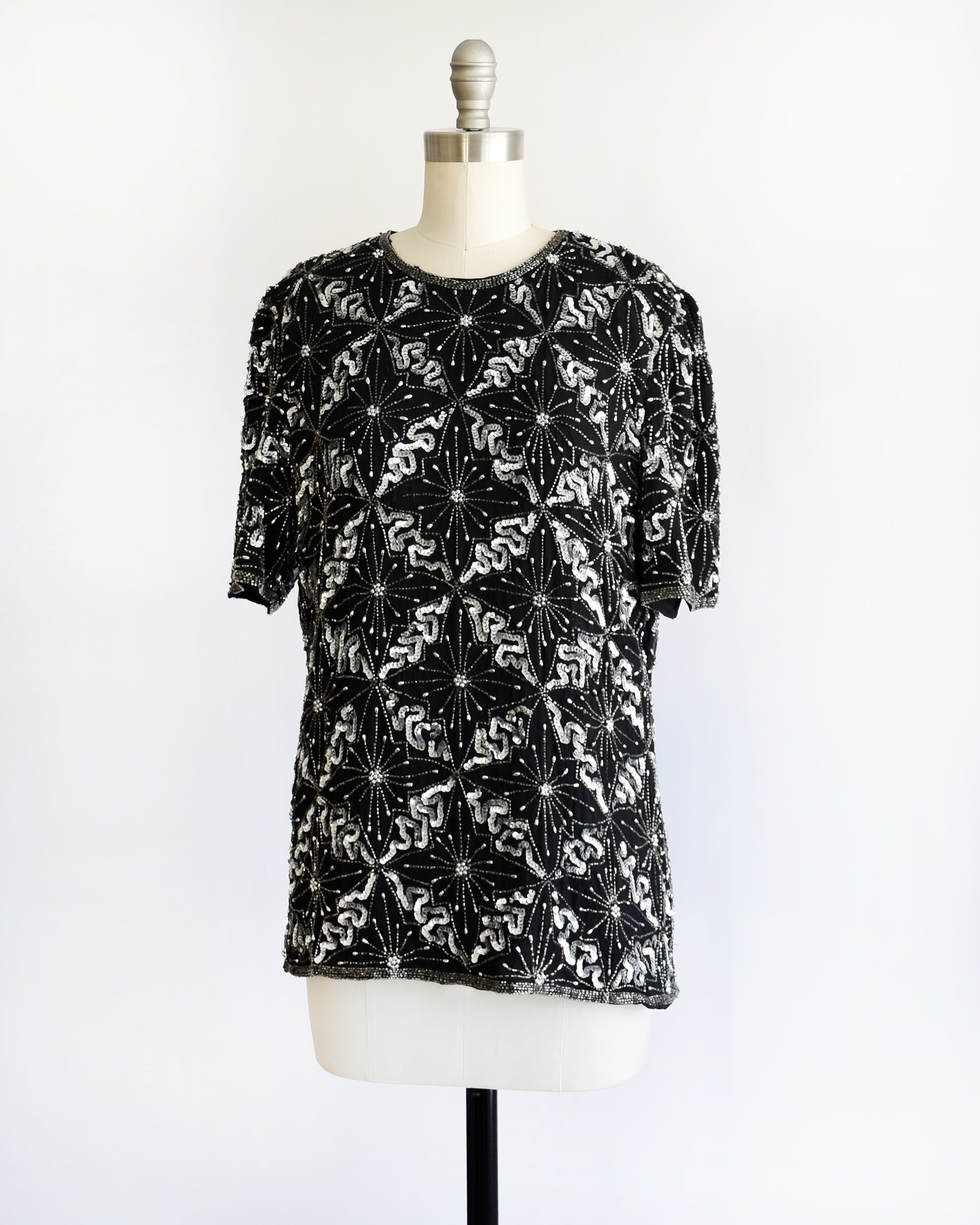 side font view of a vintage 1980s black and silver sequin beaded patterned top on a mannequin against a white background