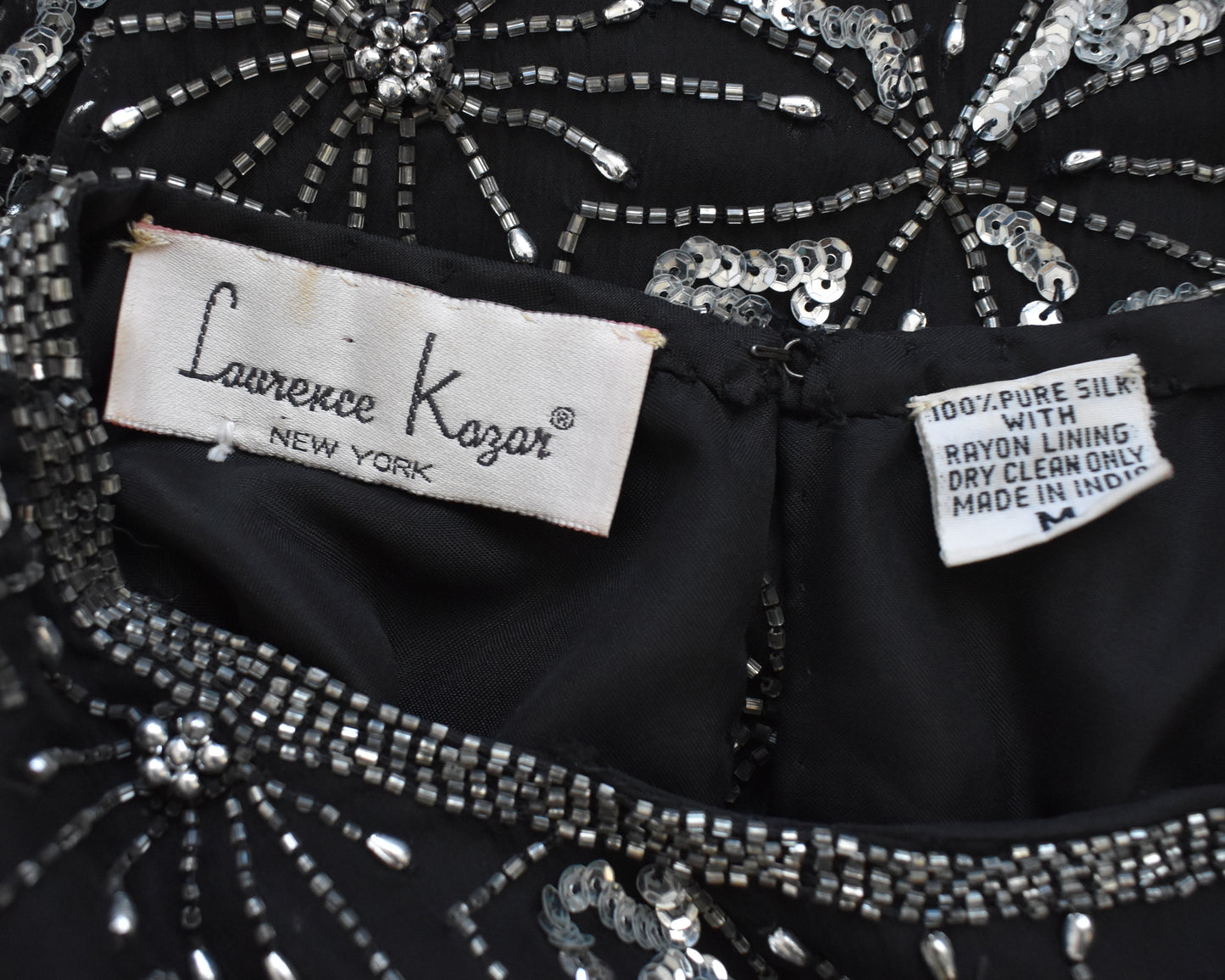 Close-up of a black garment with silver embellishments and Lawrence Kazar labels.