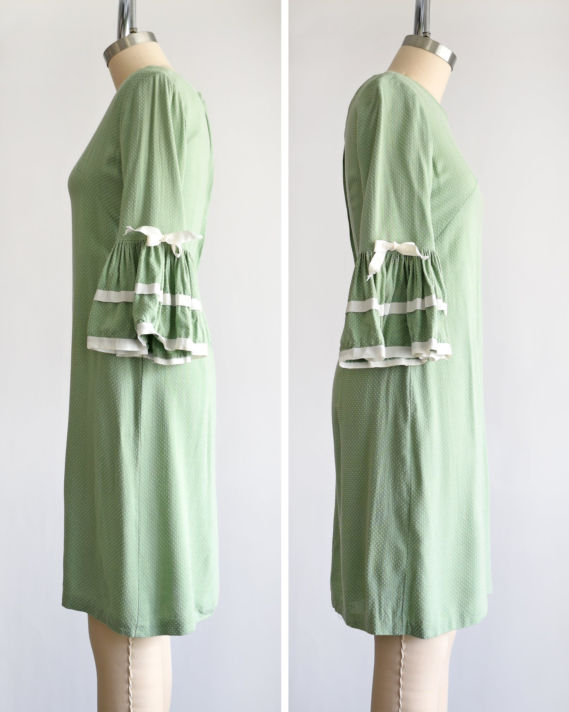 side by side views of the side of a light sage green and white Swiss dot  vintage 1960s dress displayed on a dress form mannequin against a plain white background. The dress features three-quarter bell sleeves with white ruffled trim at the cuffs.