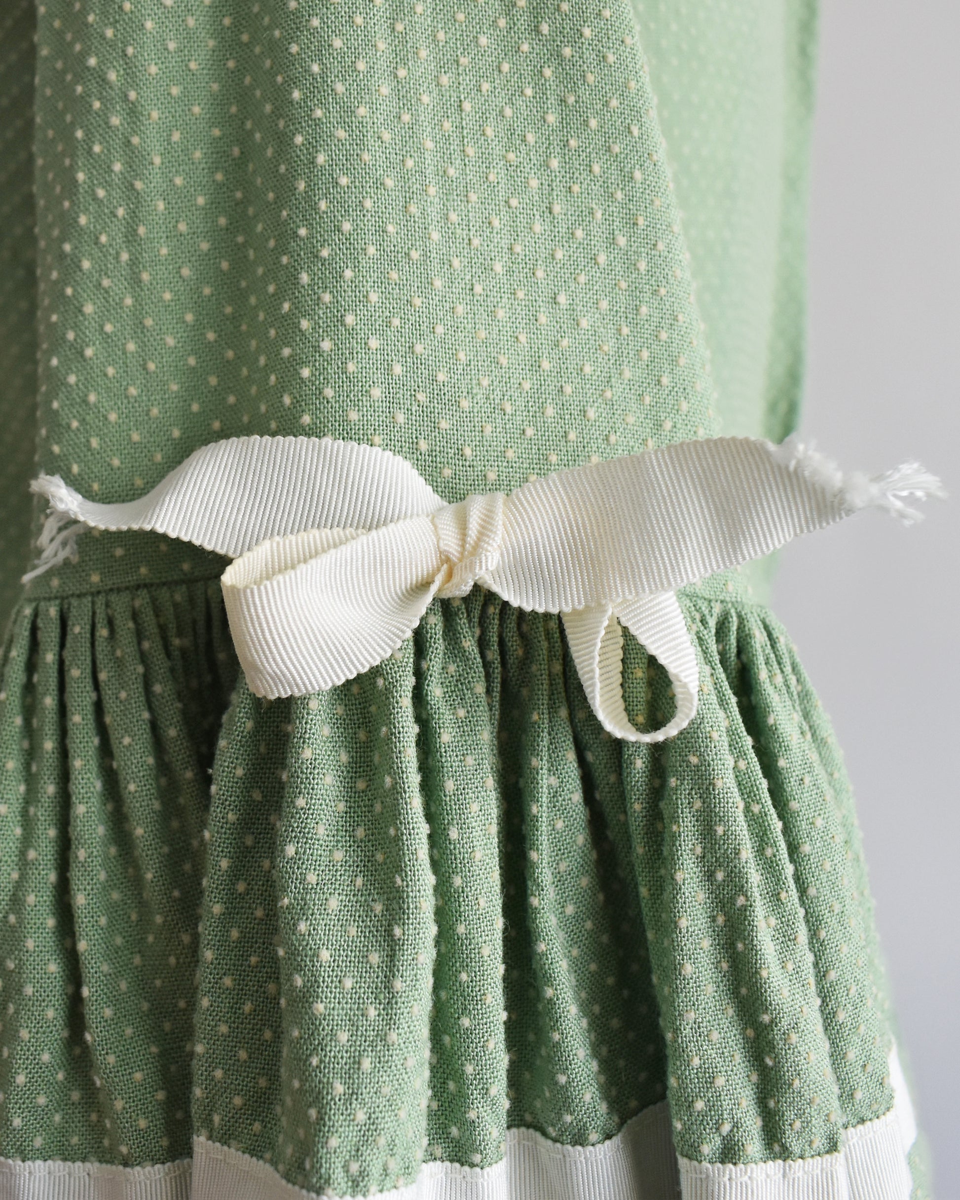 close up of the bows on the sleeves of a light sage green vintage 1960s dress displayed on a dress form mannequin against a plain white background. 