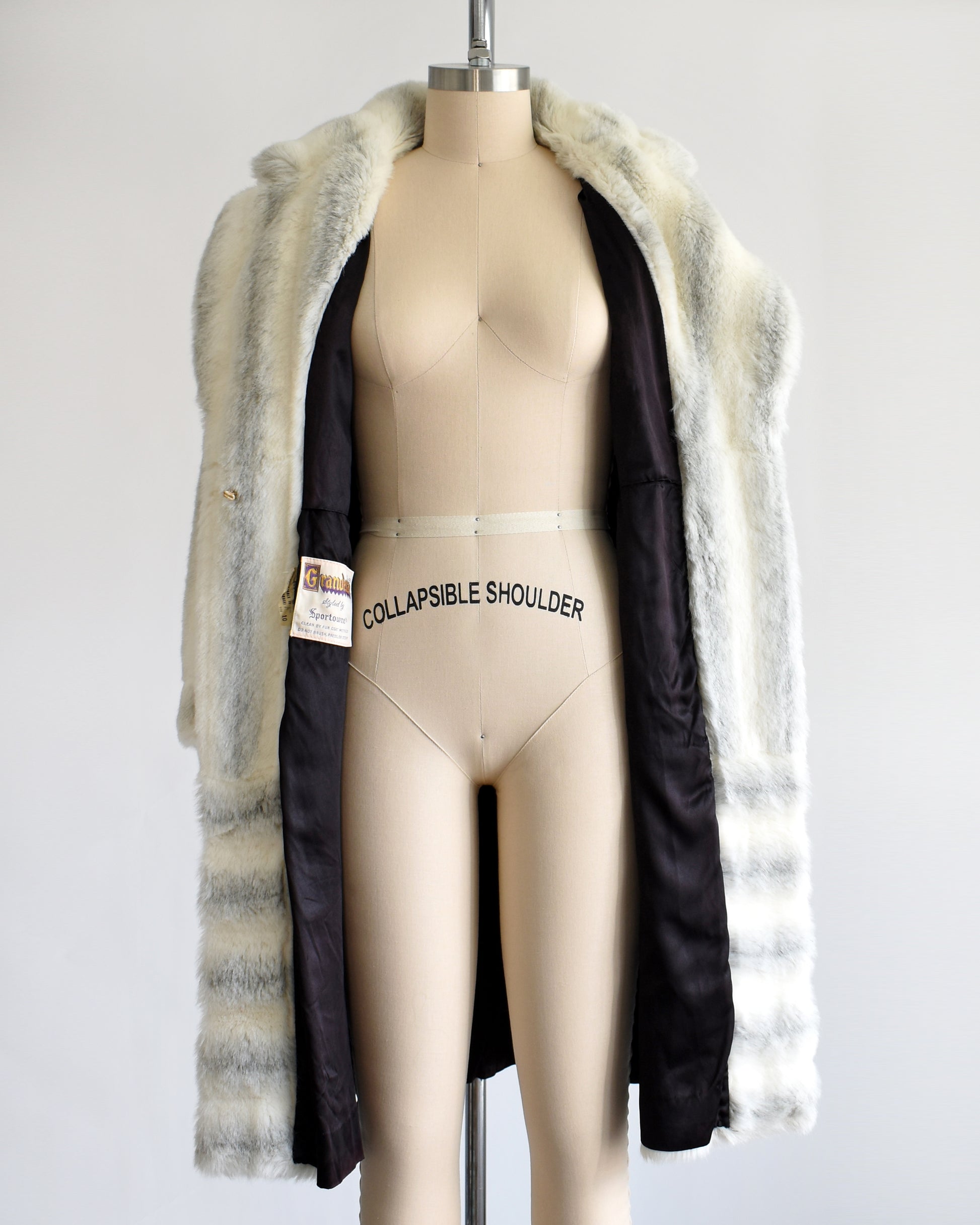 a vintage 1970s white and gray striped faux fur coat on a dress form. the coat is open showing the black lining