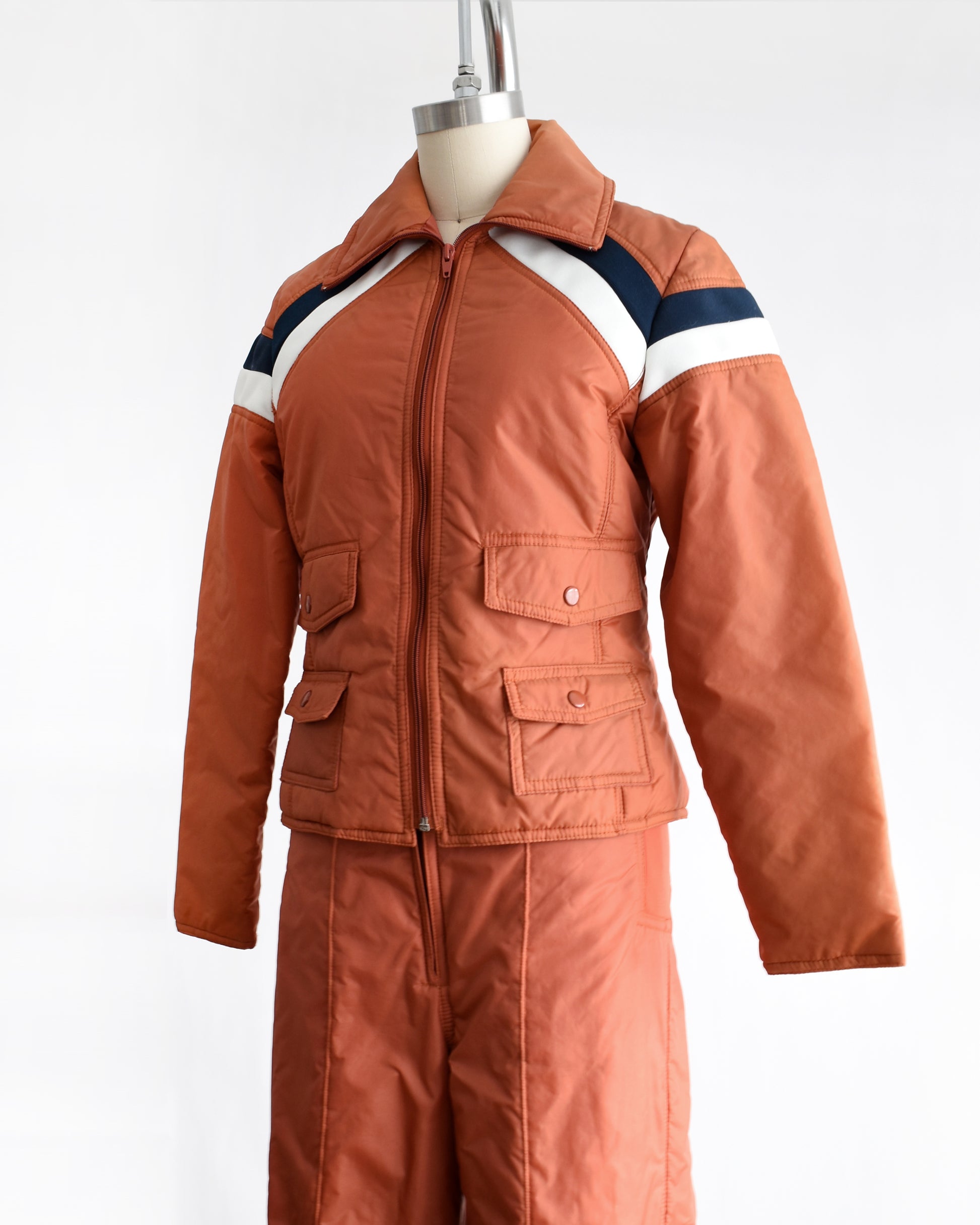 side front view of a vintage 1970s orange winter ski suit on a mannequin against a white background