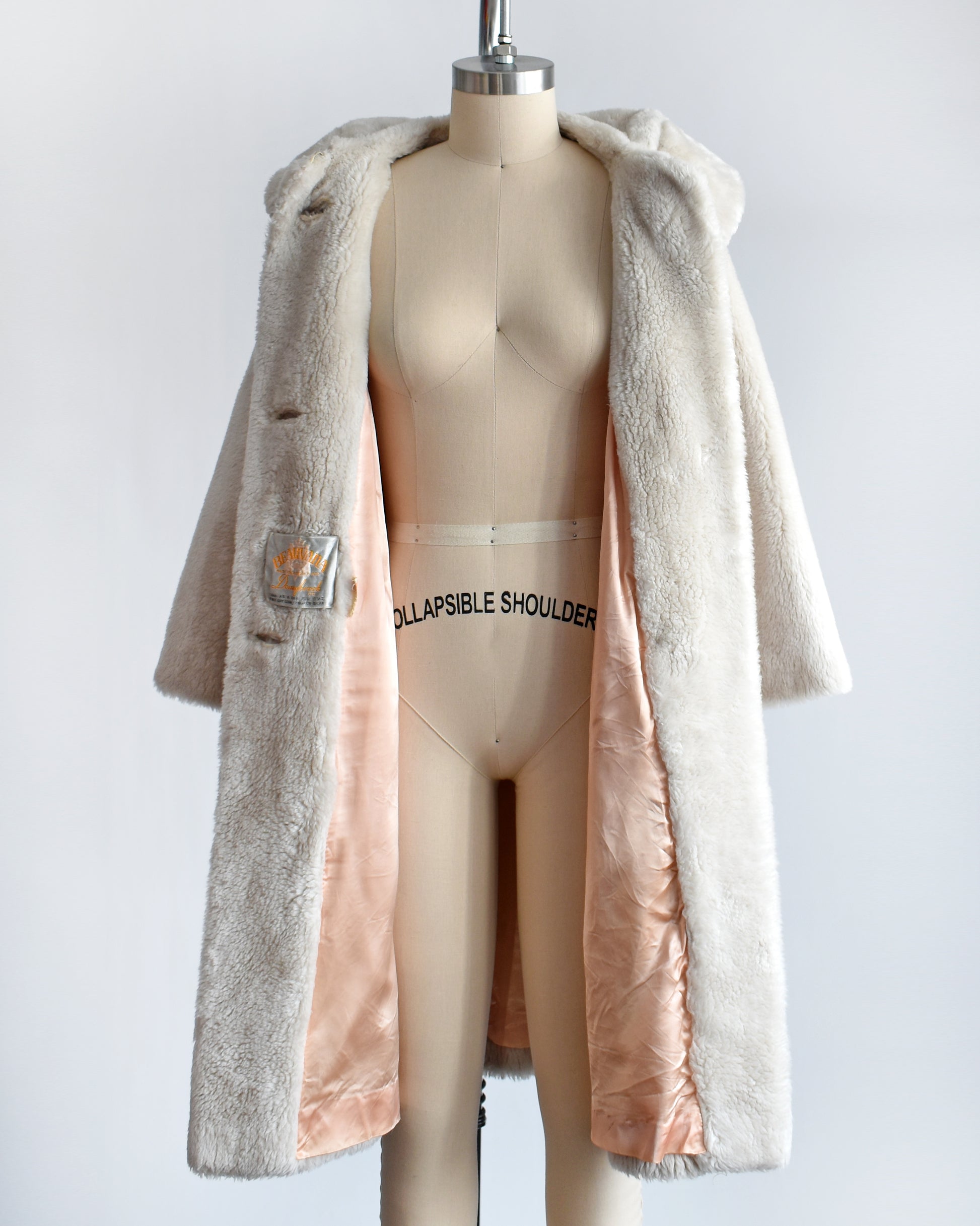 A vintage 1960s plush cream faux fur coat that features a Peter Pan style collar. The coat is open showing the peachy lining