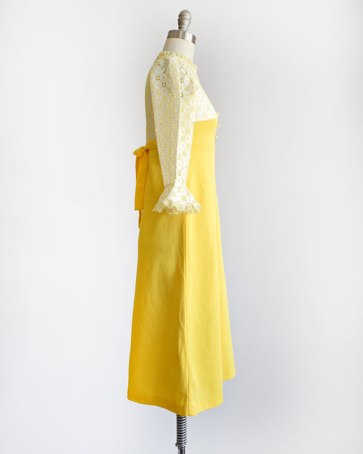 side view of a vintage 1960s white and yellow lace mod babydoll dress with three rhinestone buttons on a dress form.