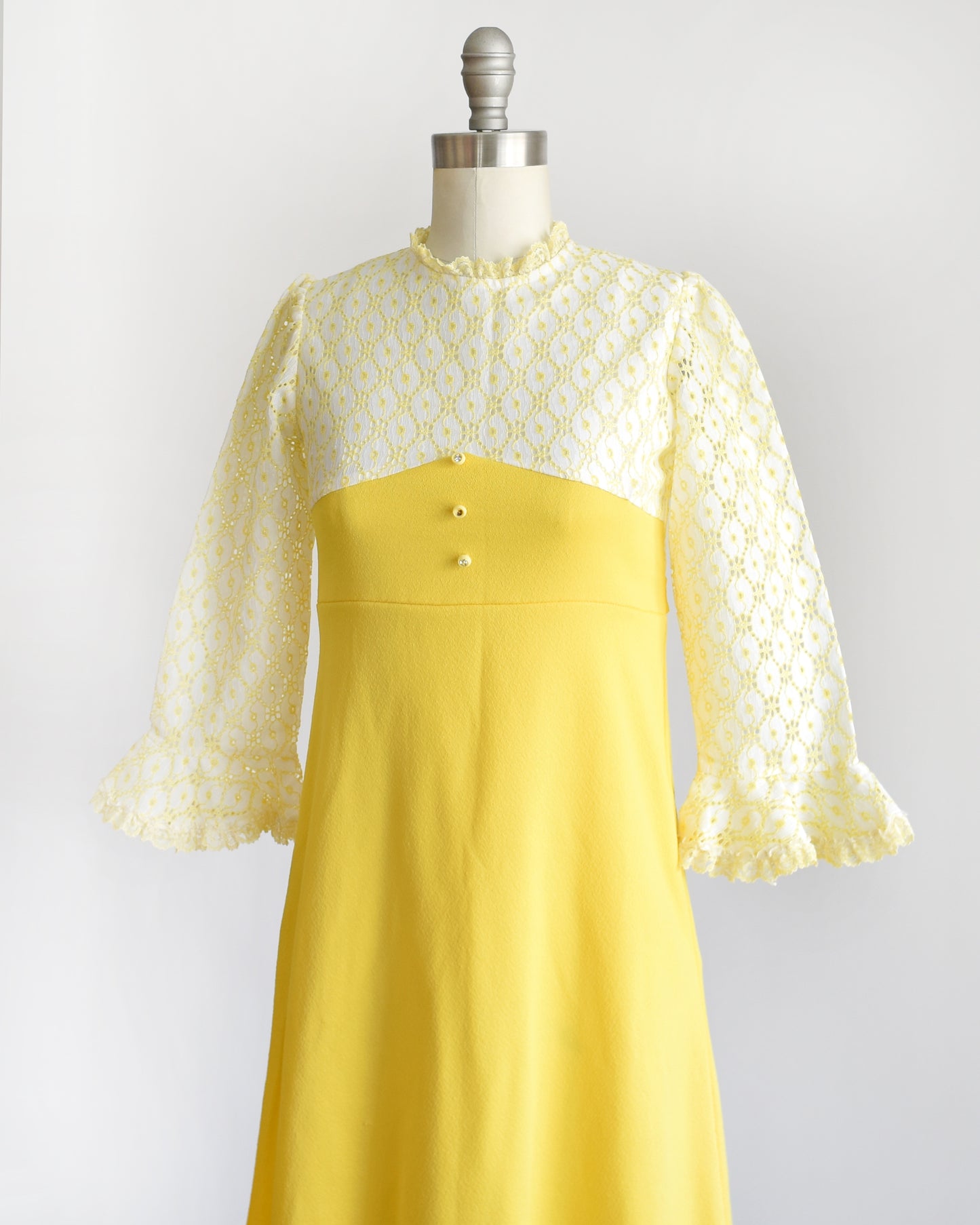 side front view of a vintage 1960s white and yellow lace mod babydoll dress with three rhinestone buttons on a dress form.