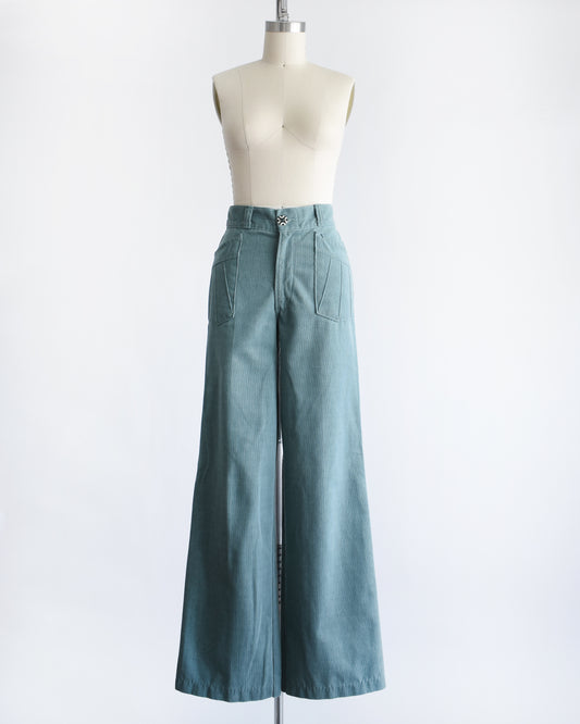 A pair of vintage 1970s high-waisted, wide-leg pants in a muted teal blue-green color, displayed on a cream-colored dress form mannequin against a plain white background.
