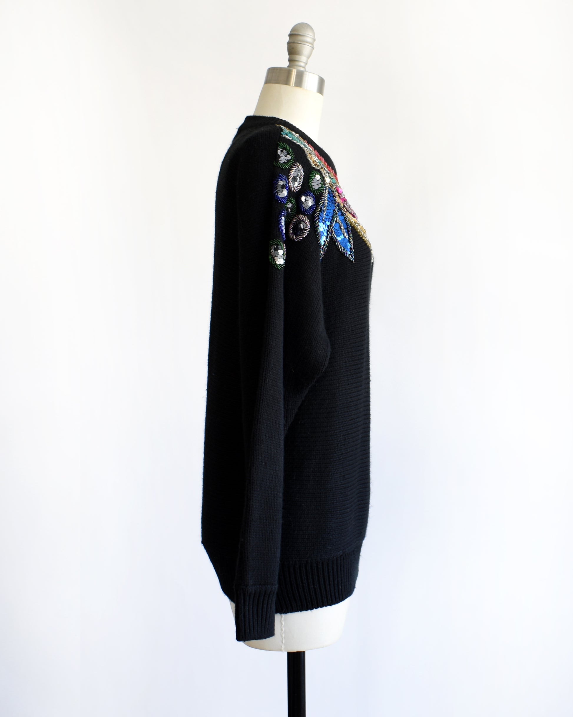 side view of a vintage 1980s black sweater with colorful floral sequin and beaded detail on a mannequin against a white background
