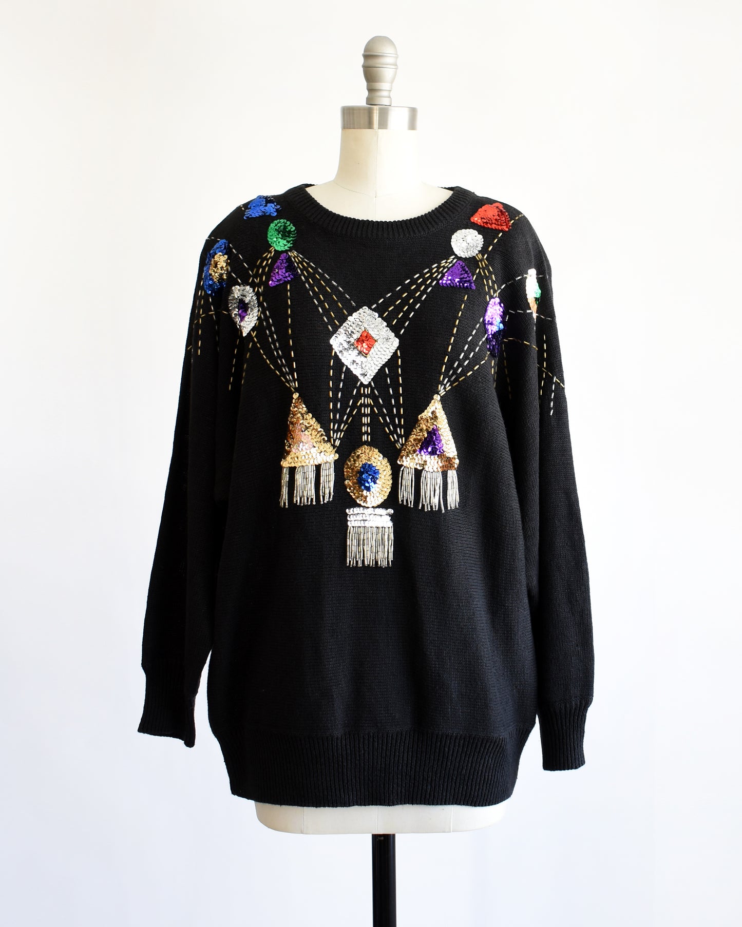 a vintage black sweater with colorful gemstone sequins and tassel details on a mannequin against a white background