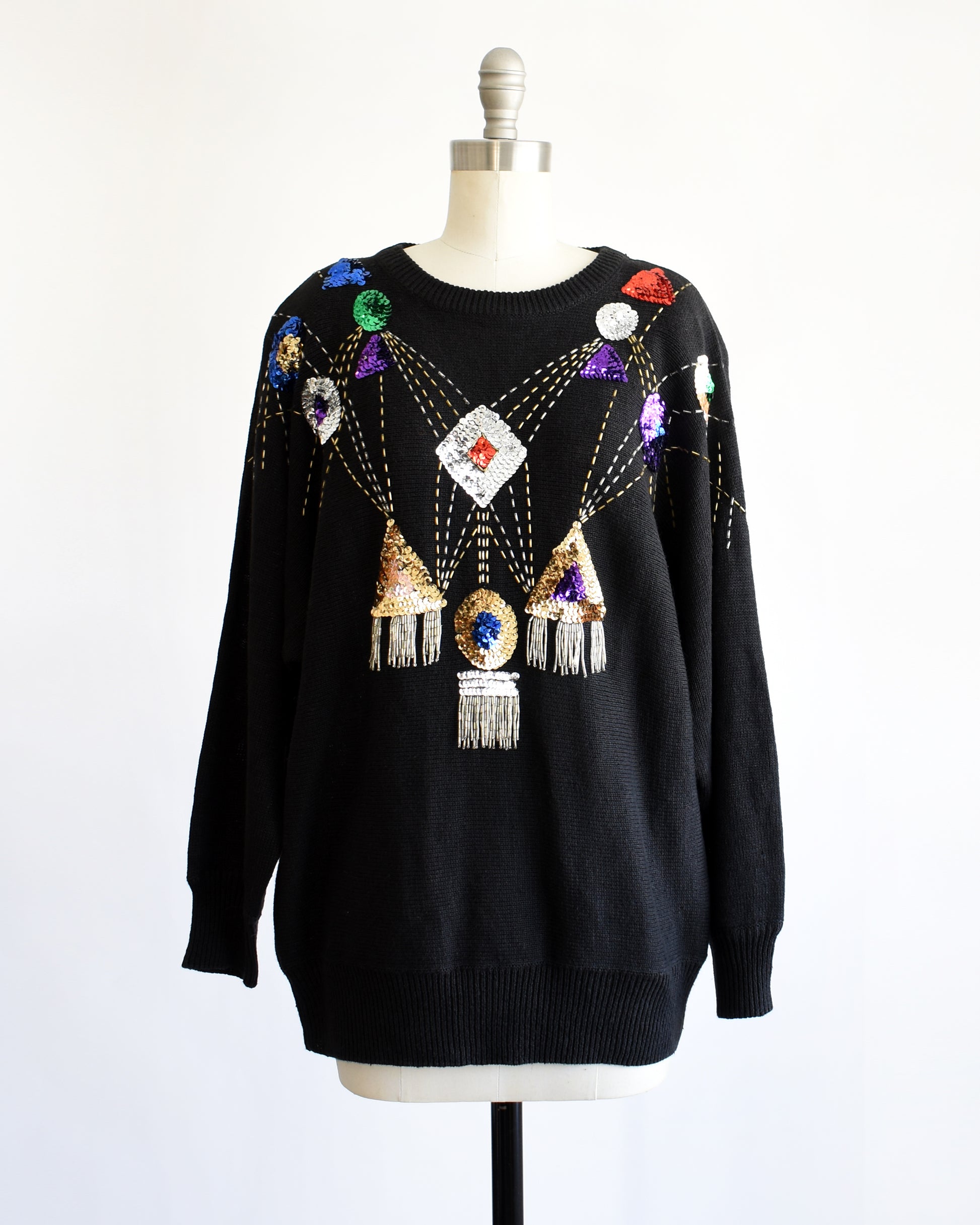 a vintage black sweater with colorful gemstone sequins and tassel details on a mannequin against a white background