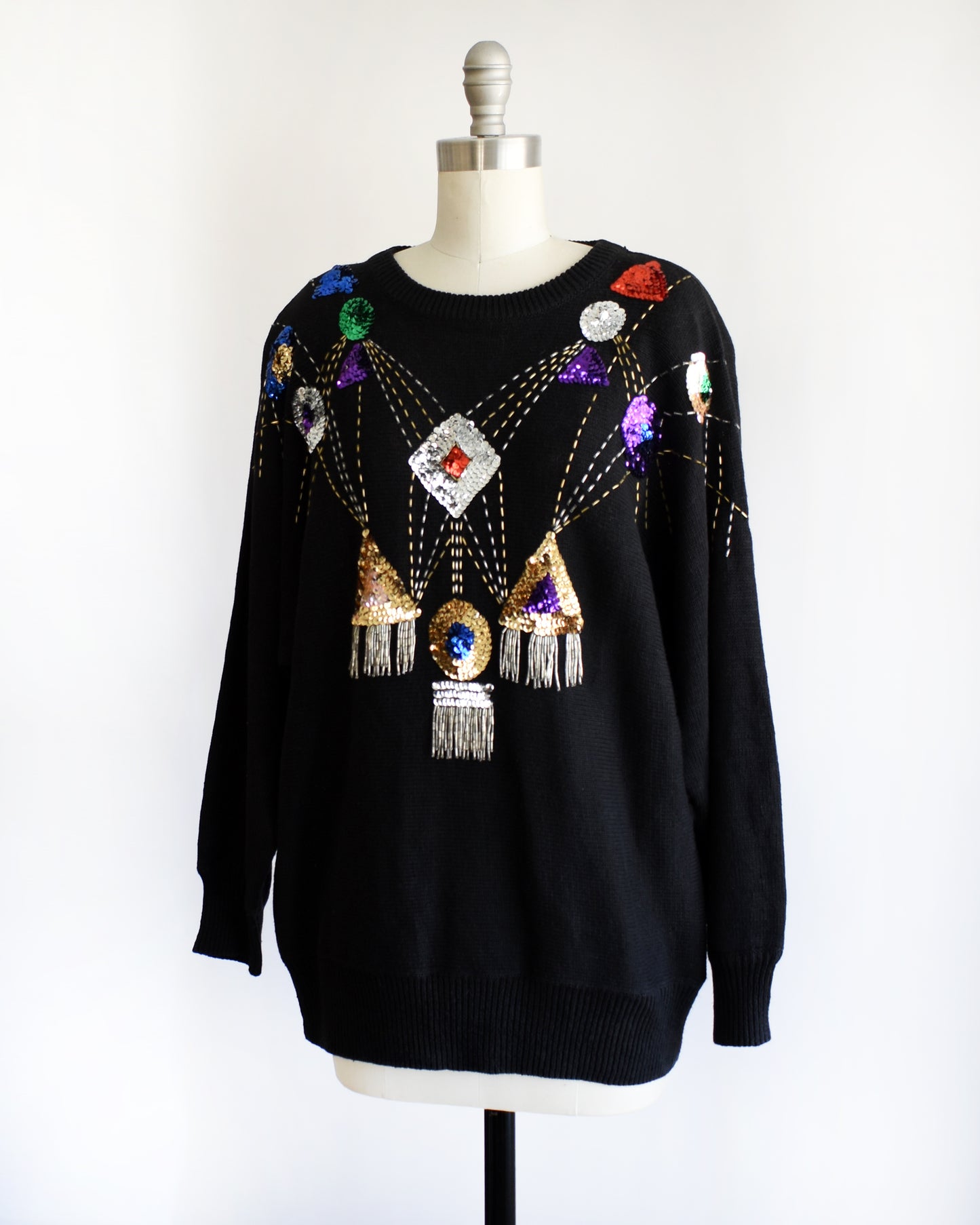 side front view of a vintage black sweater with colorful gemstone sequins and tassel details on a mannequin against a white background