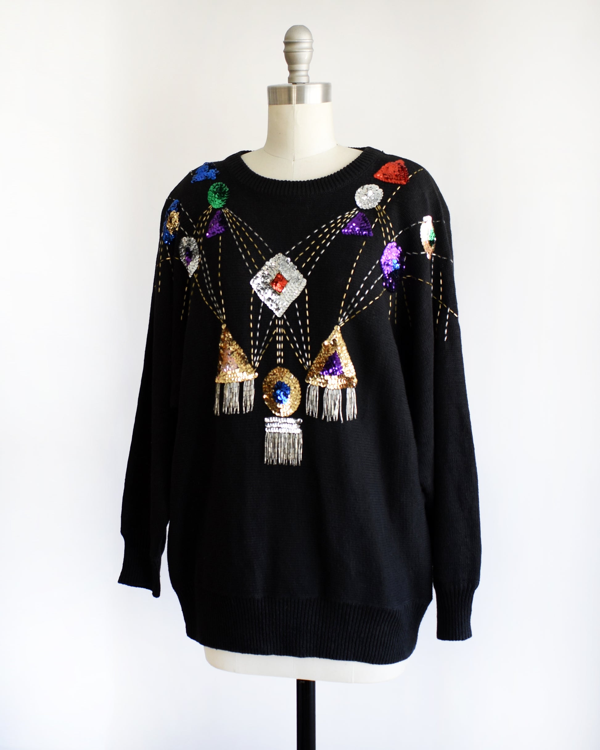 side front view of a vintage black sweater with colorful gemstone sequins and tassel details on a mannequin against a white background